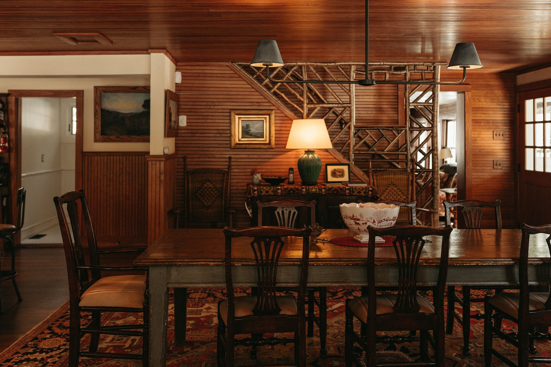 A dining room with a long table and chairs and a lamp.