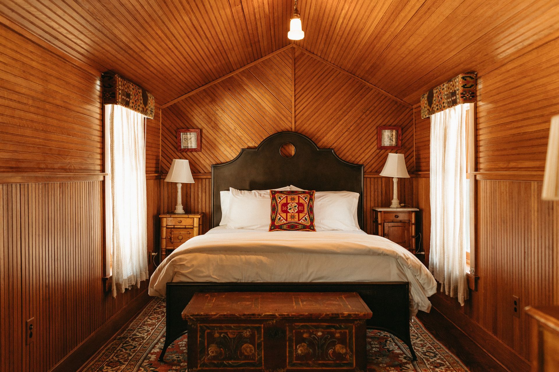 A bedroom with a bed , nightstands , lamps and a trunk.
