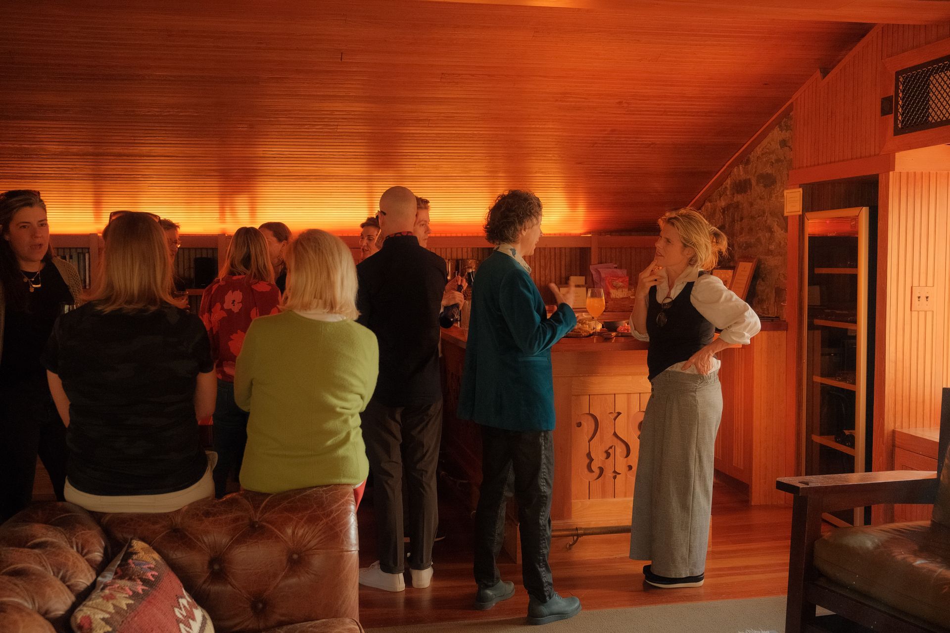 A group of people are standing around a bar in a living room.