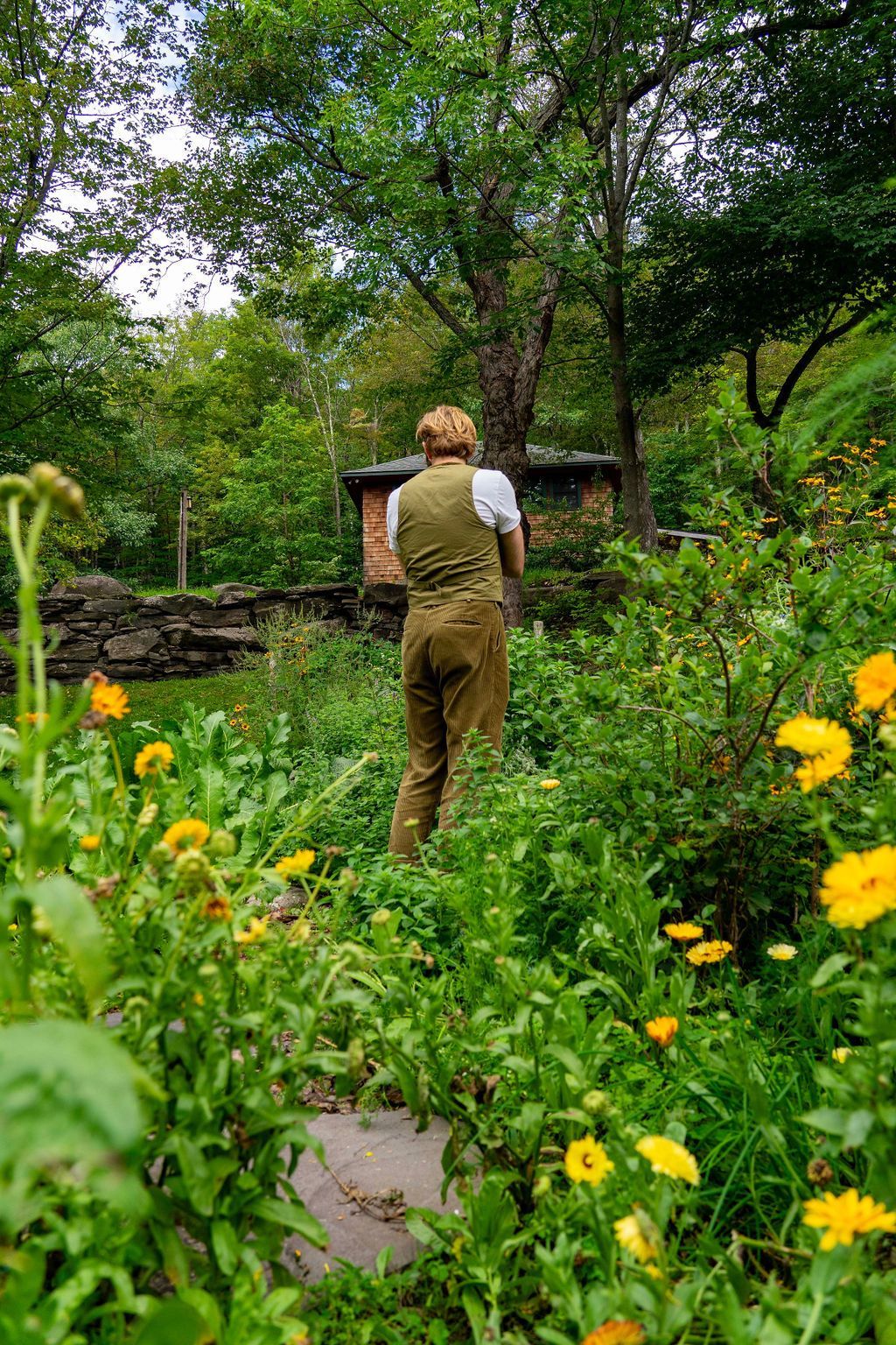 A man is standing in a garden surrounded by flowers and trees.