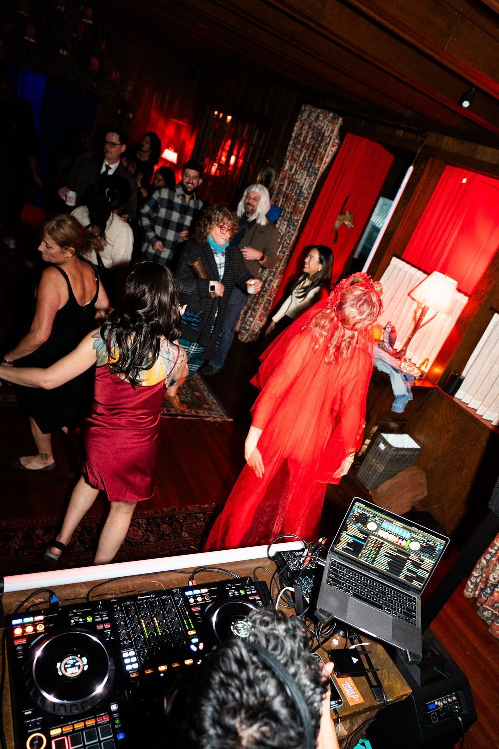 A group of people are dancing in a room with a dj and a laptop.