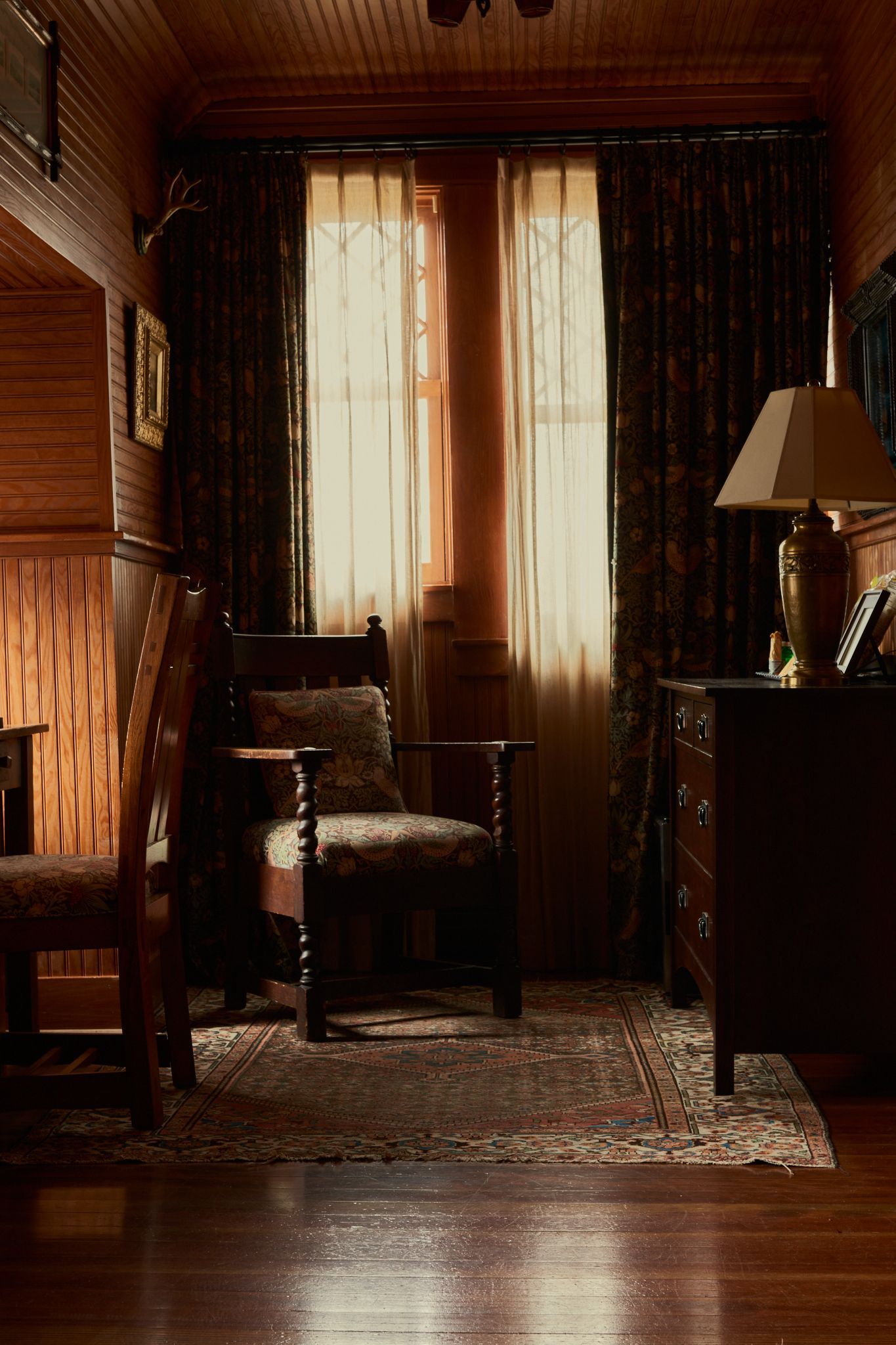 A living room with a chair a dresser and a lamp
