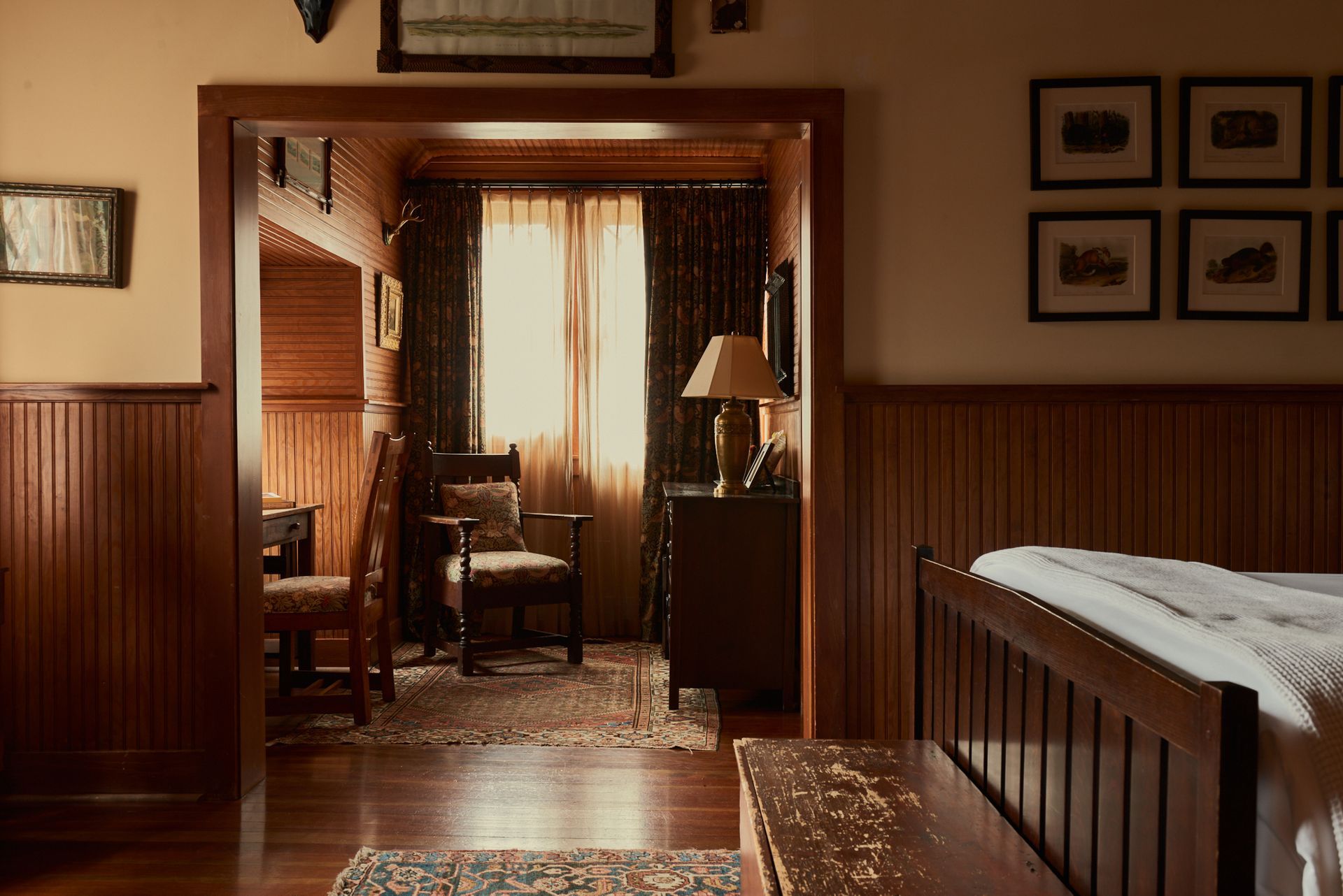 A bedroom with wood paneling , a bed , chairs , and a lamp.
