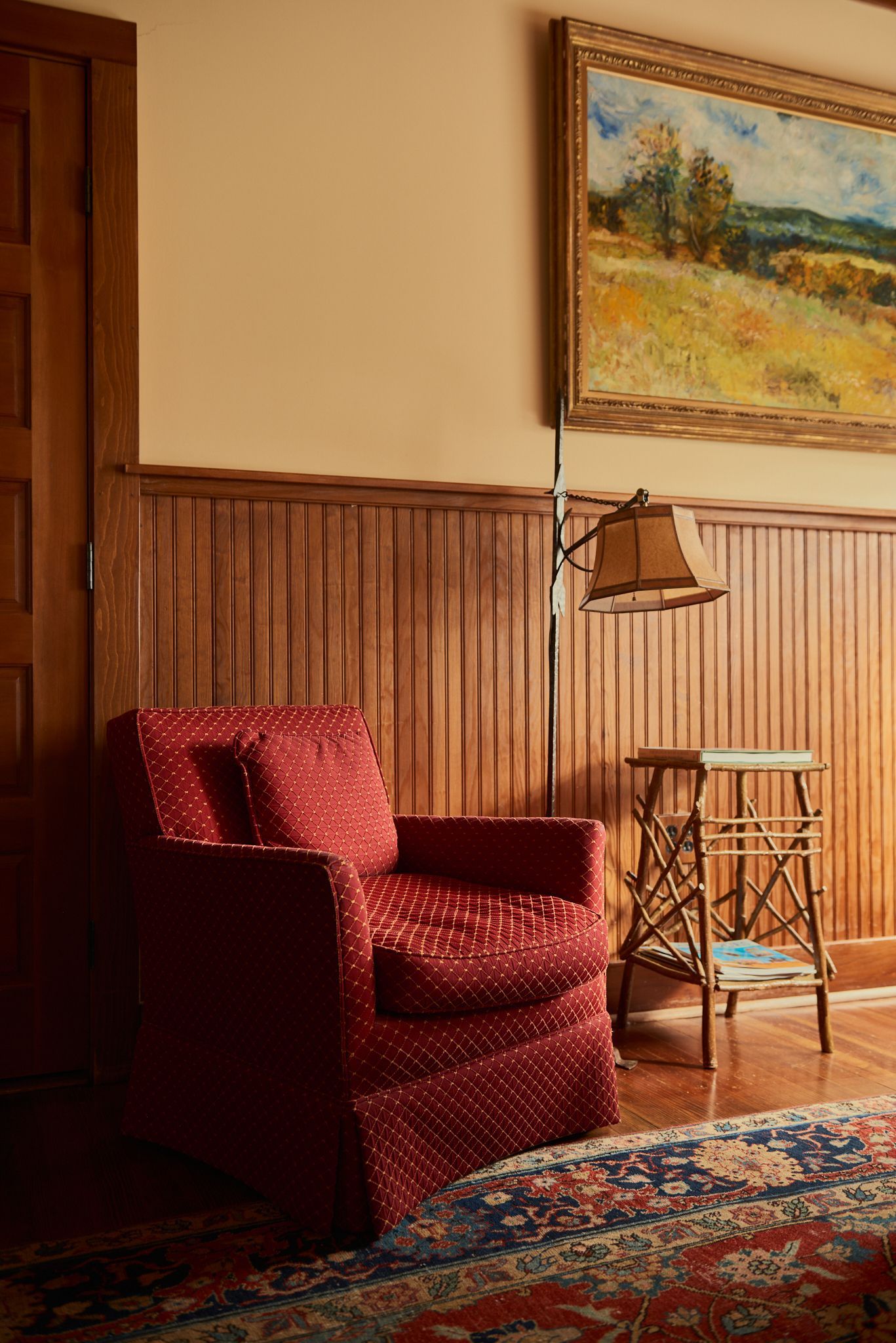 A living room with a red chair and a painting on the wall.