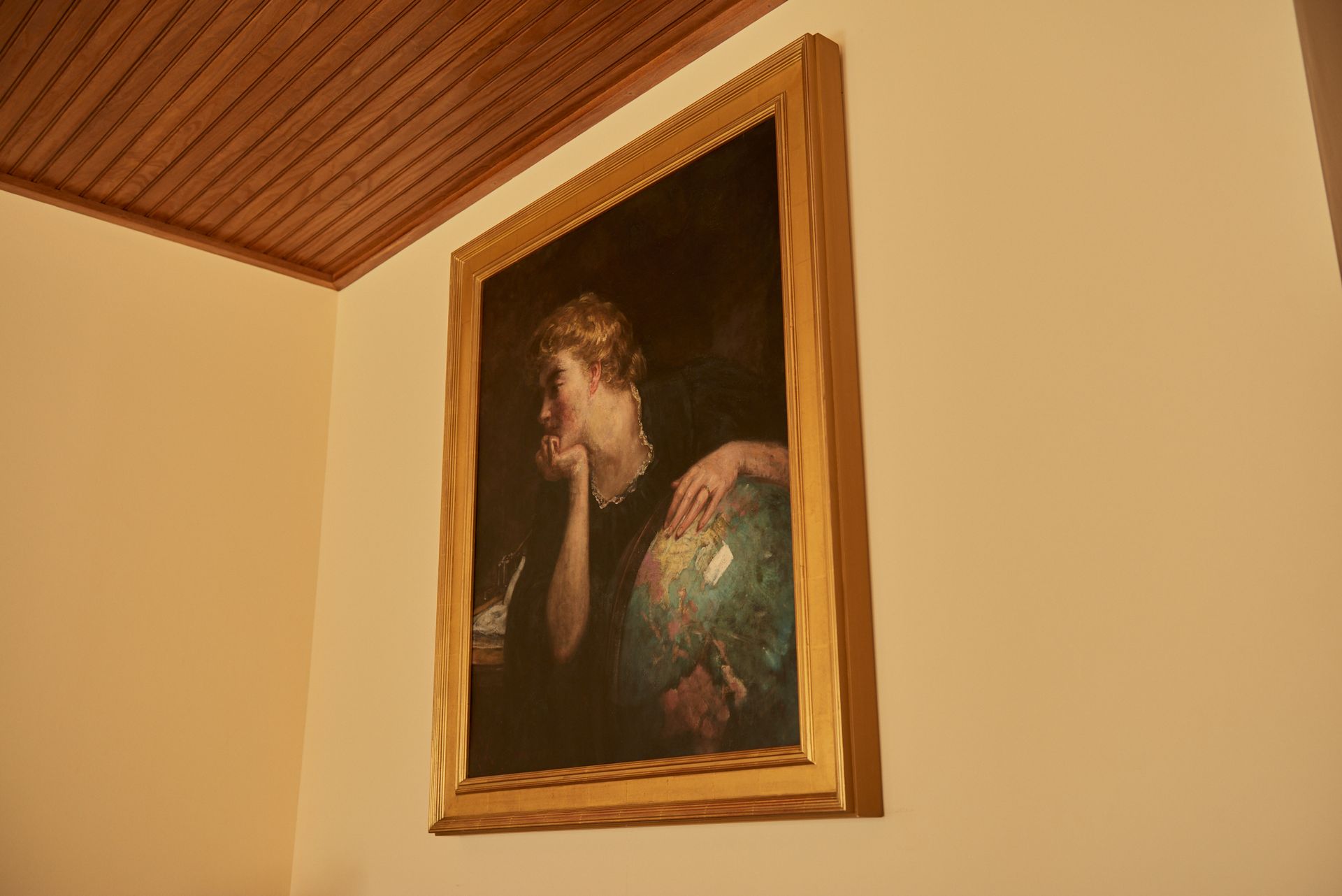 A painting of a woman holding a globe is hanging on a wall.