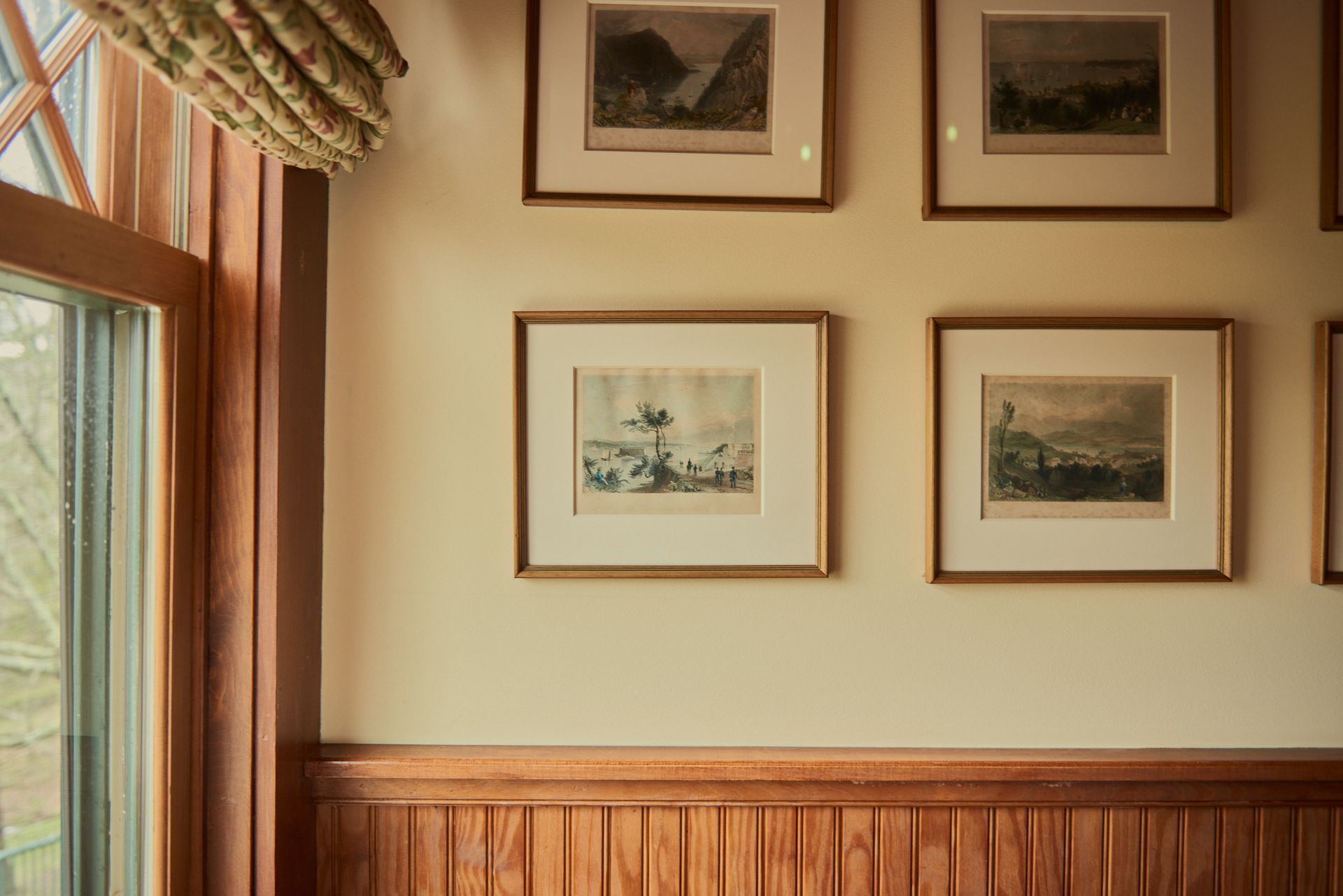 A row of framed pictures are hanging on a wall next to a window.