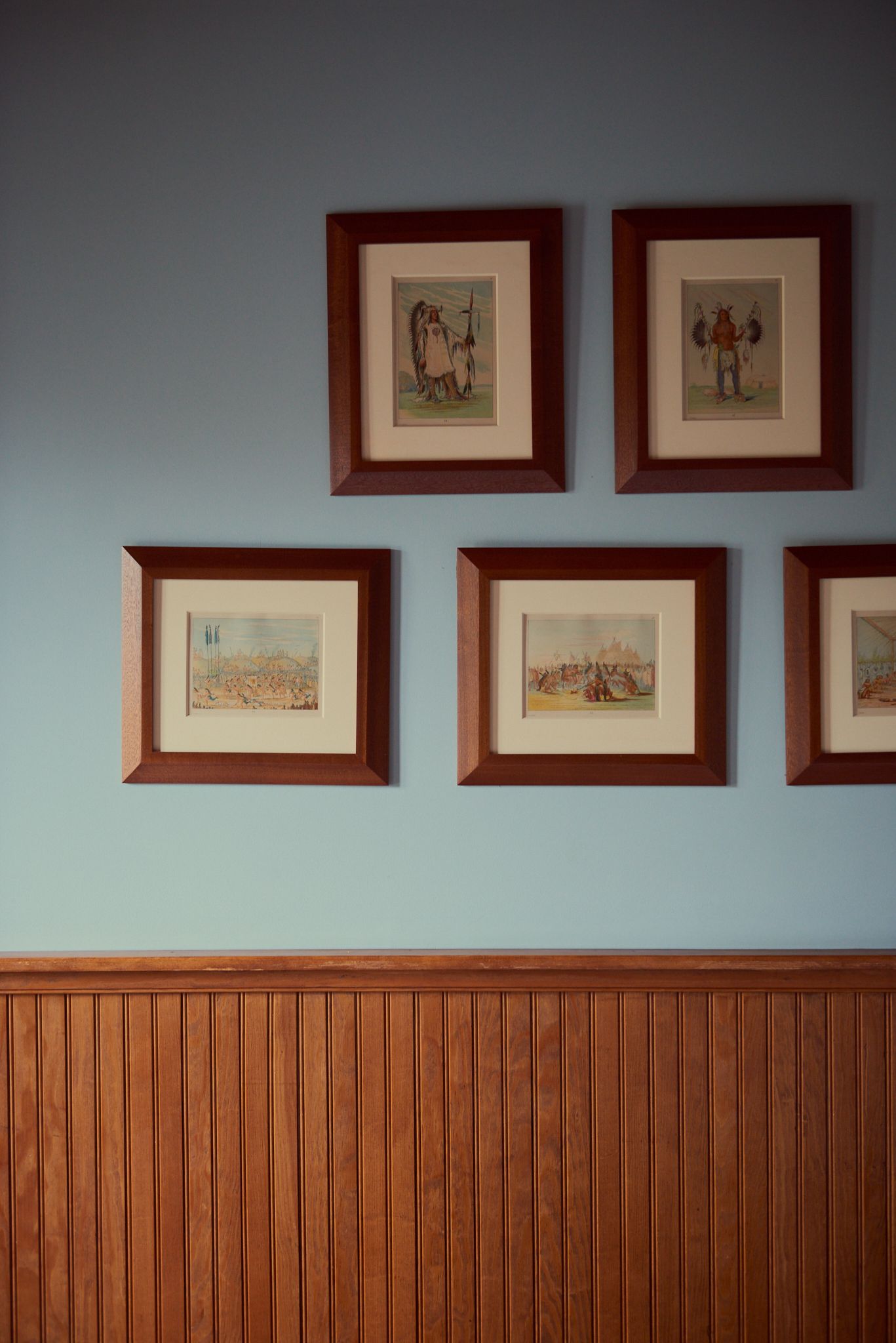 Four framed pictures are hanging on a wall with wood paneling.