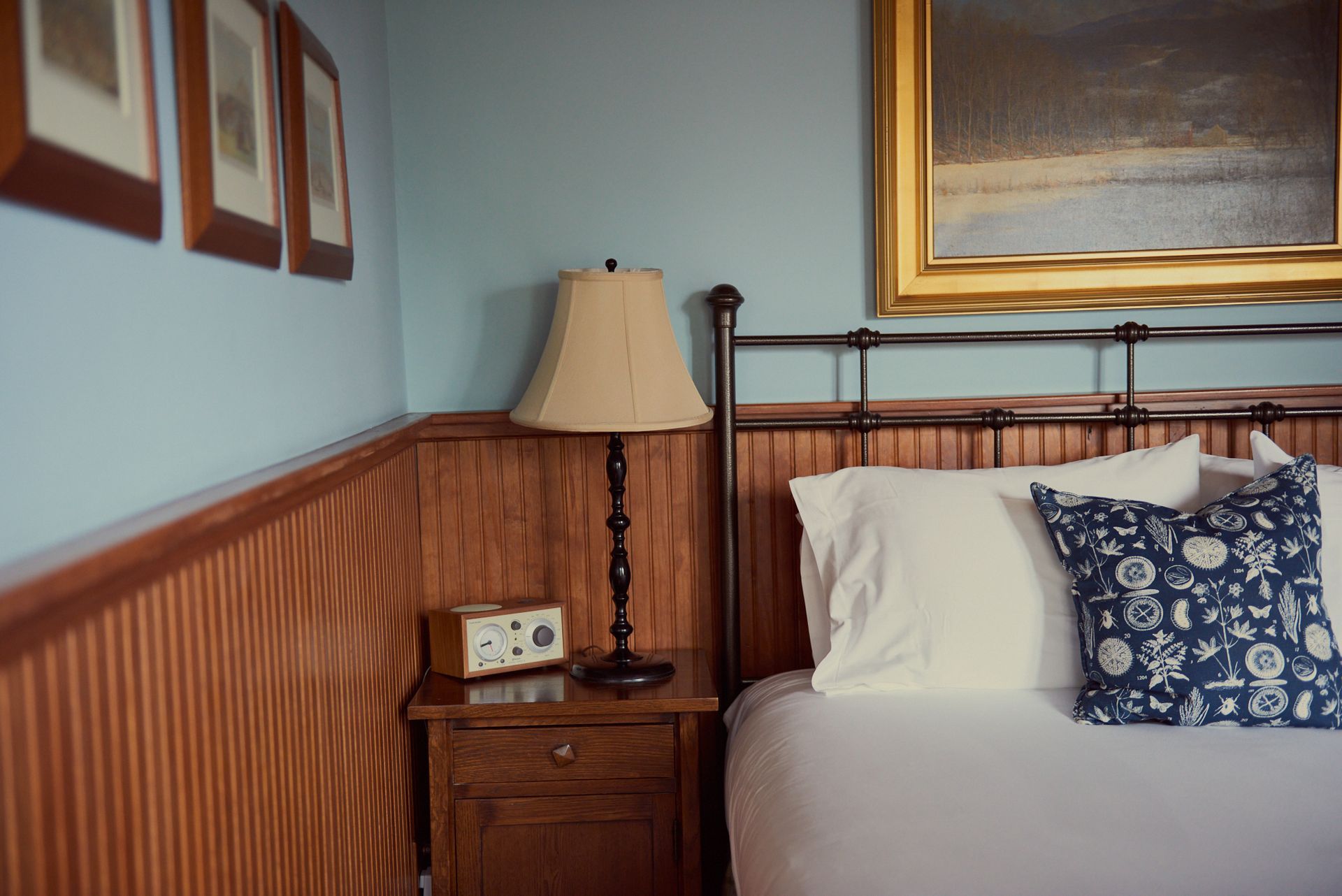 A bedroom with a bed , nightstand , lamp and painting on the wall.