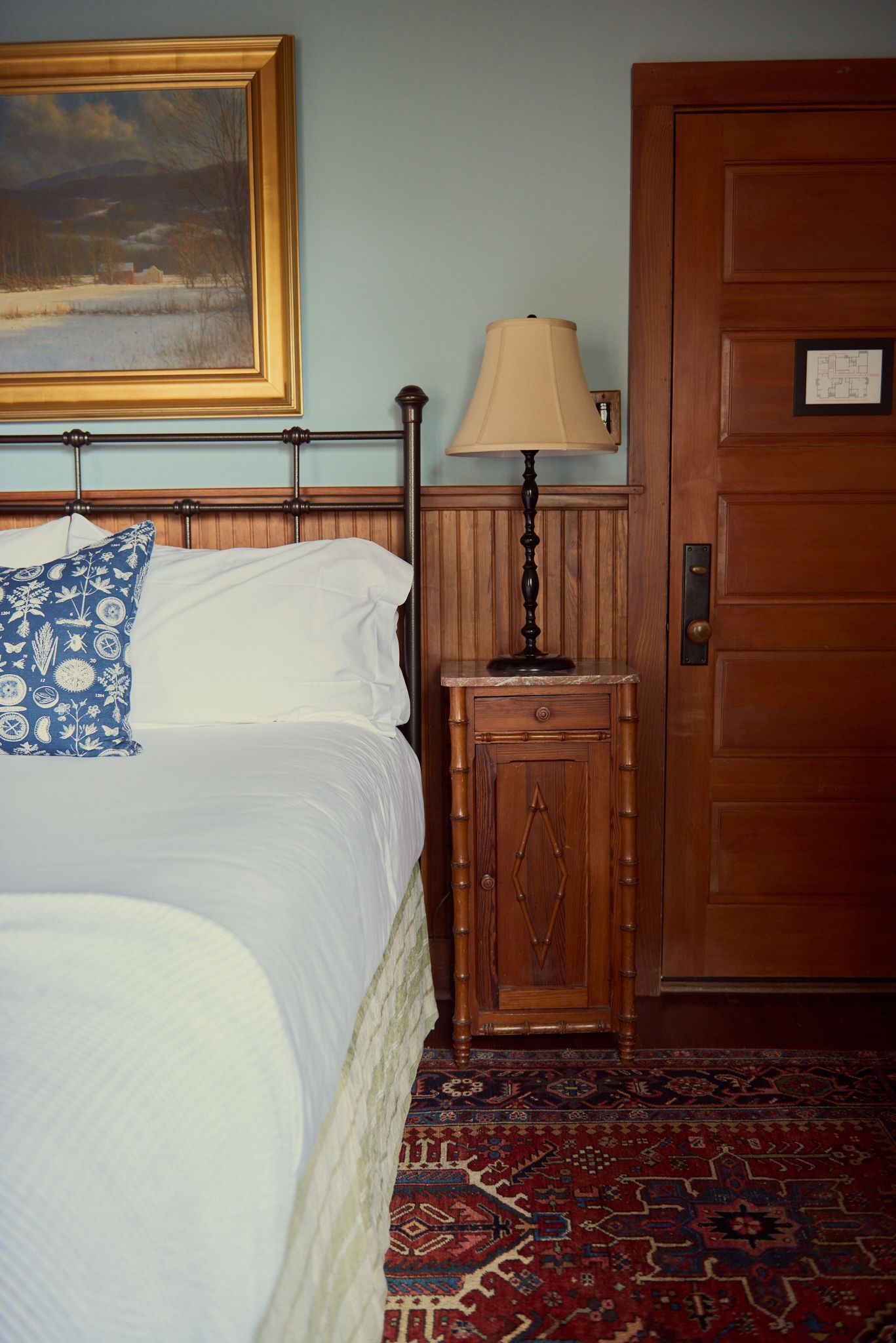 A bedroom with a bed , nightstand , lamp and painting on the wall.