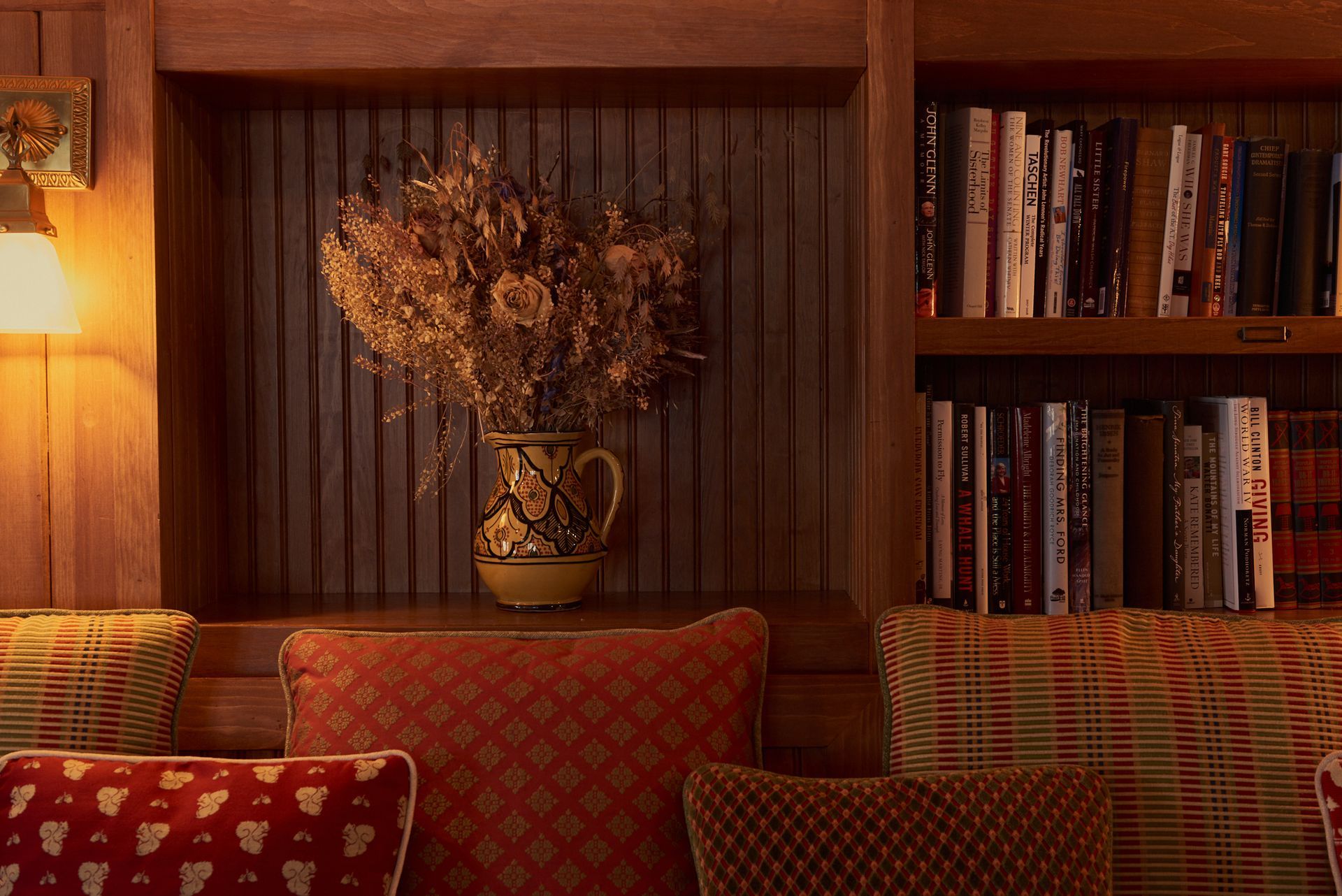 A vase of dried flowers is sitting on a shelf next to a bookshelf filled with books.