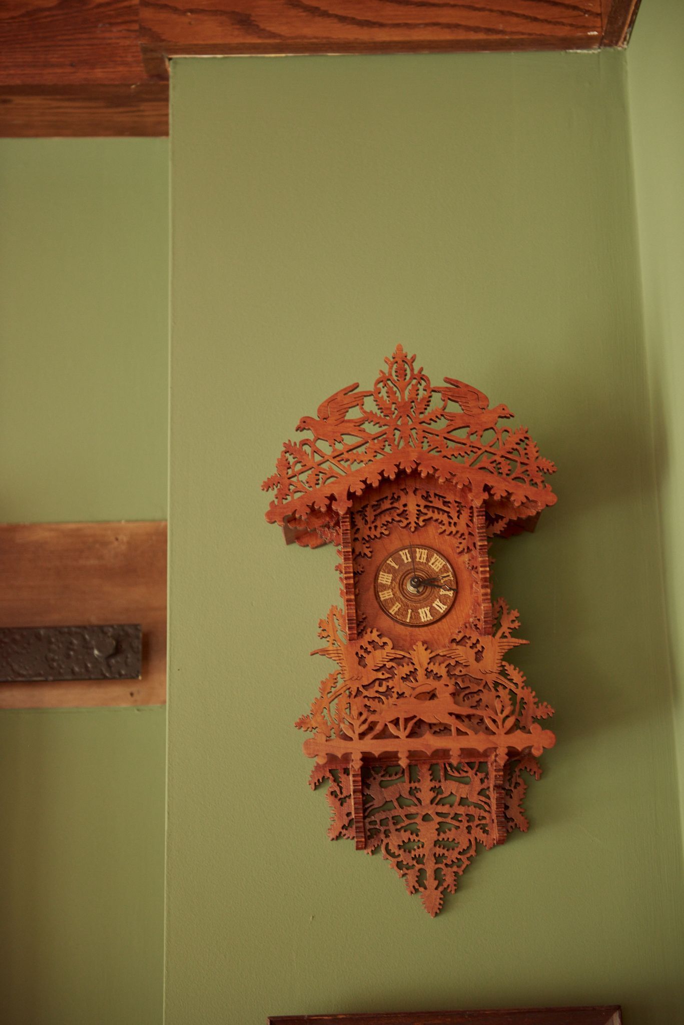 A wooden clock is hanging on a green wall.