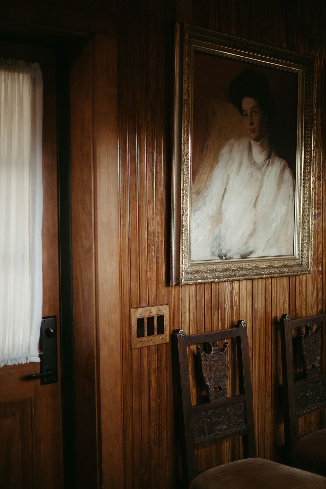 A painting of a woman in a white dress is hanging on a wooden wall.