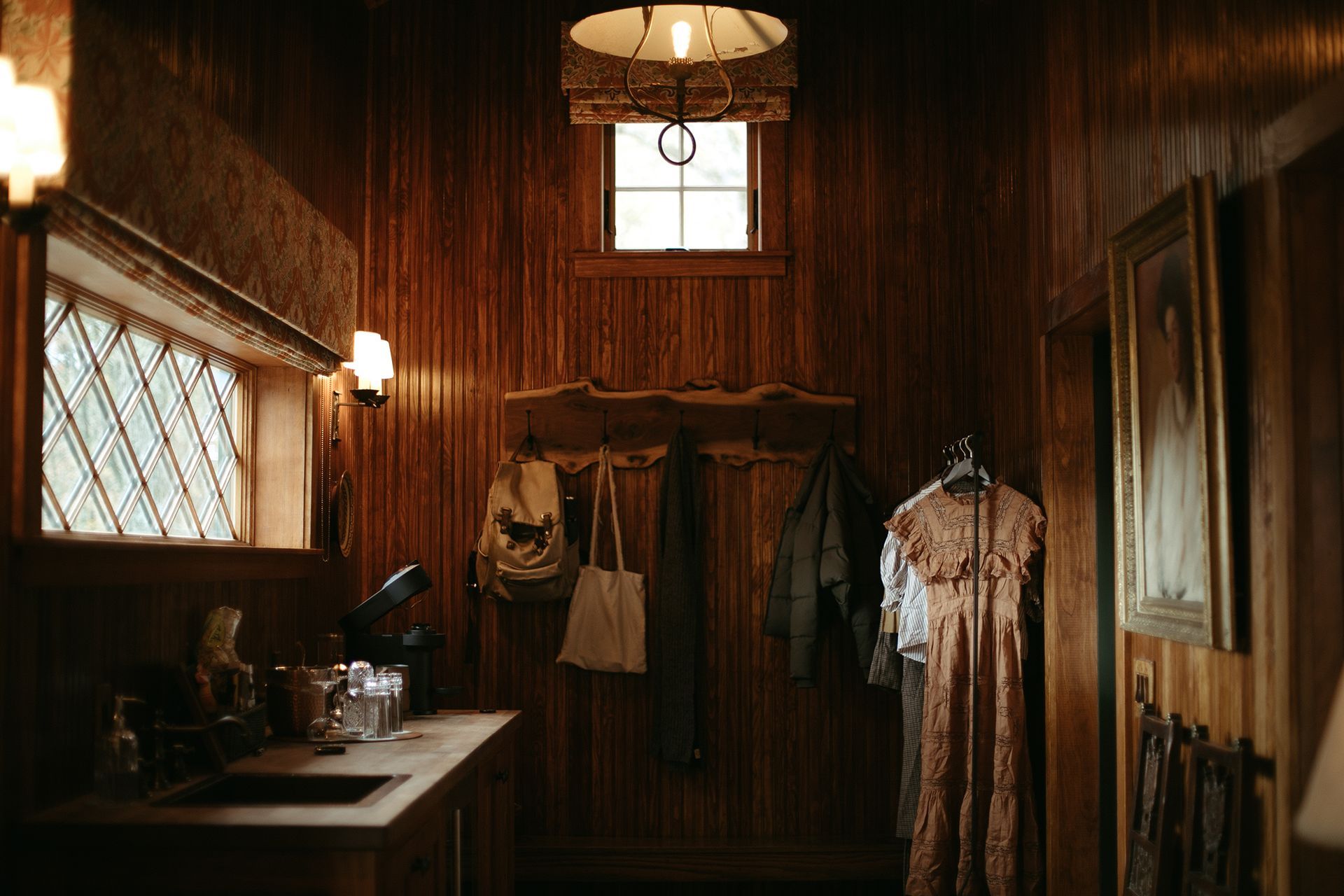 A wooden room with a sink and clothes hanging on the wall.