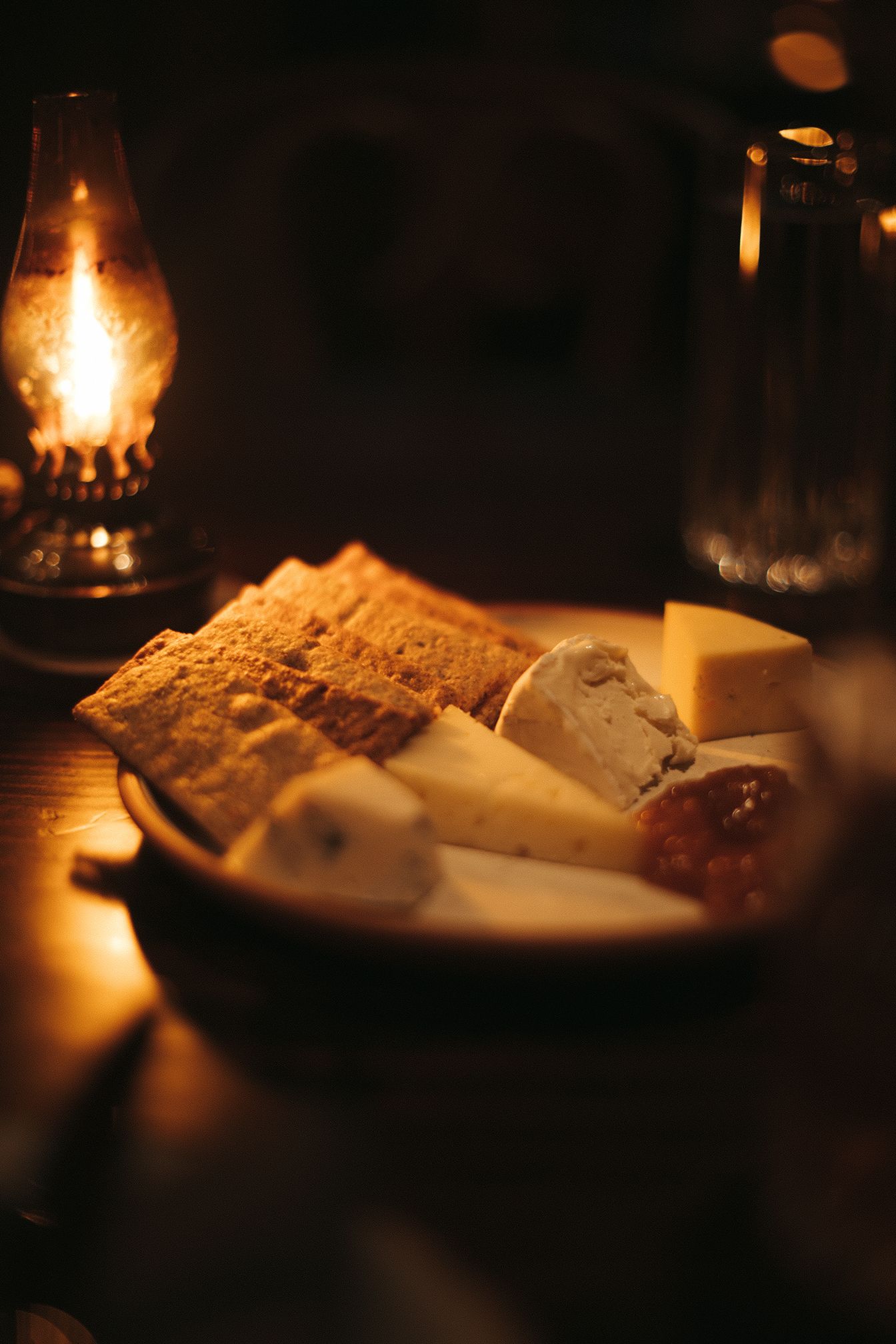 A bowl of cheese and crackers on a table with a lantern in the background.