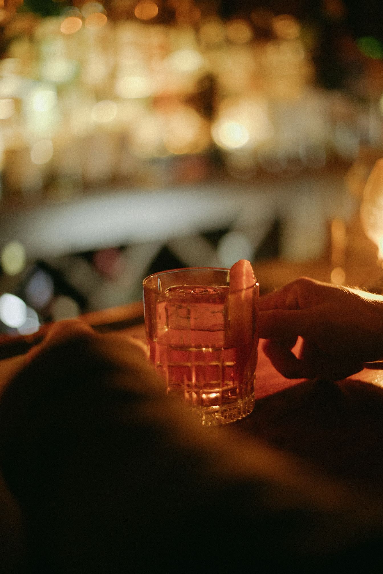 A person is holding a glass of alcohol with ice cubes in it.