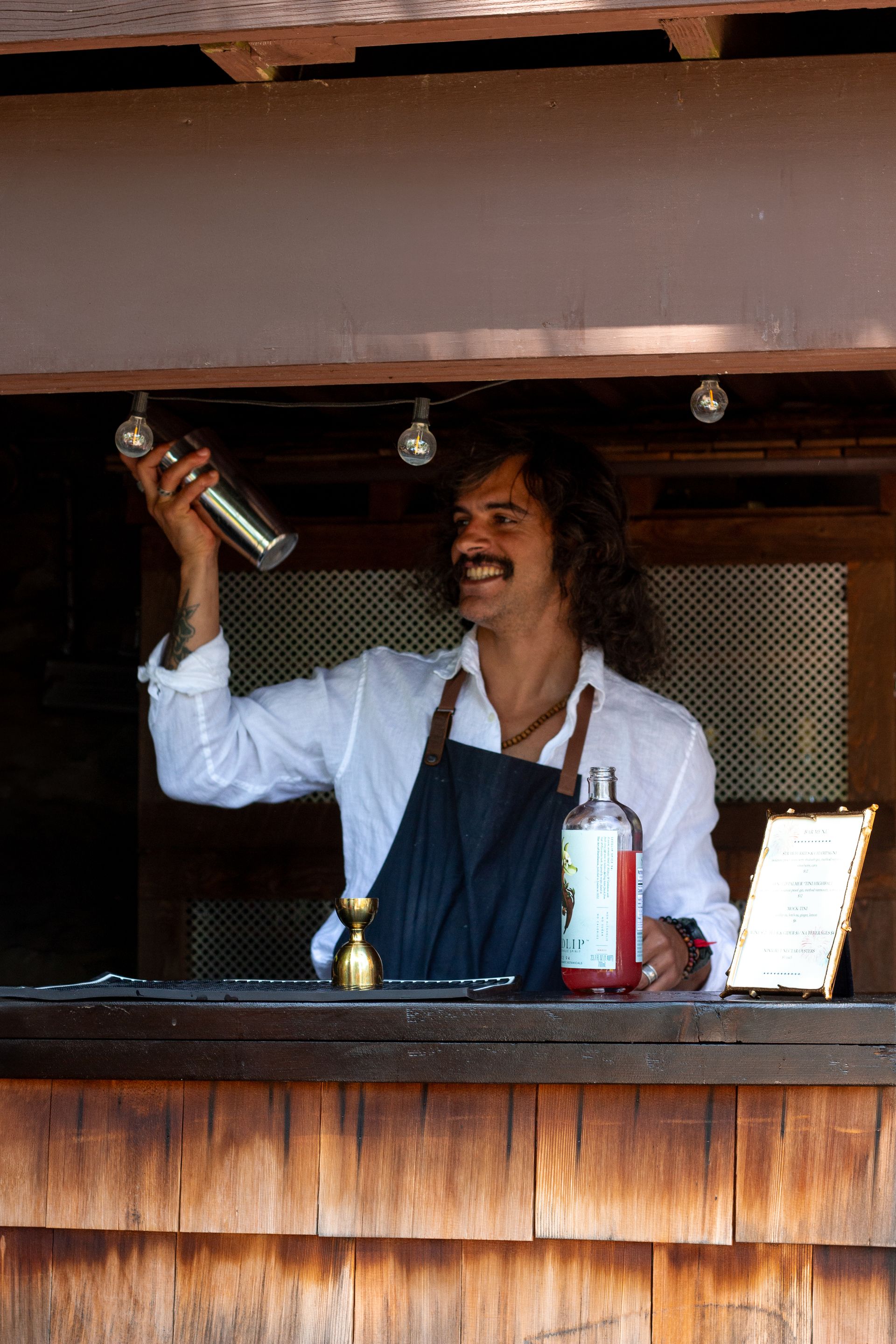 Bartender smiling while shaking a cocktail shaker behind a wooden bar