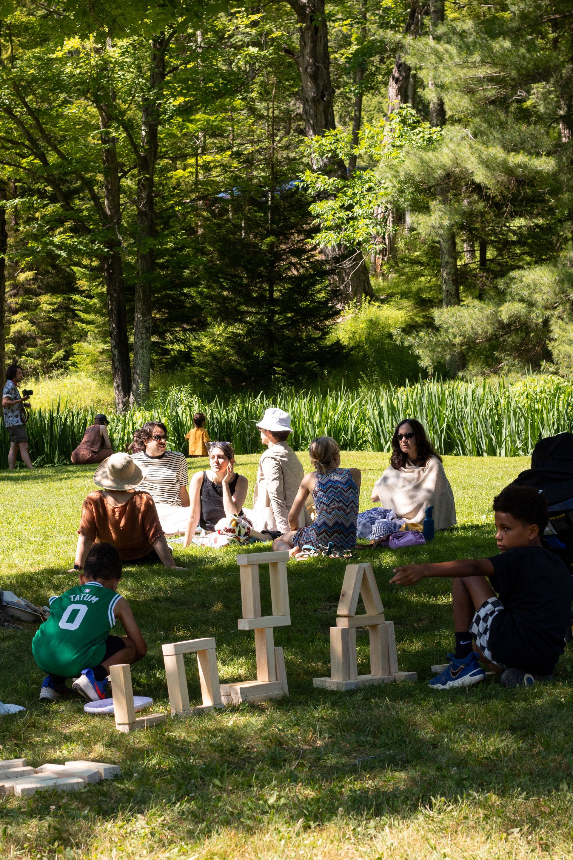 Group of people seated outdoors in a sunny park, gathered around large wooden letters on the grass