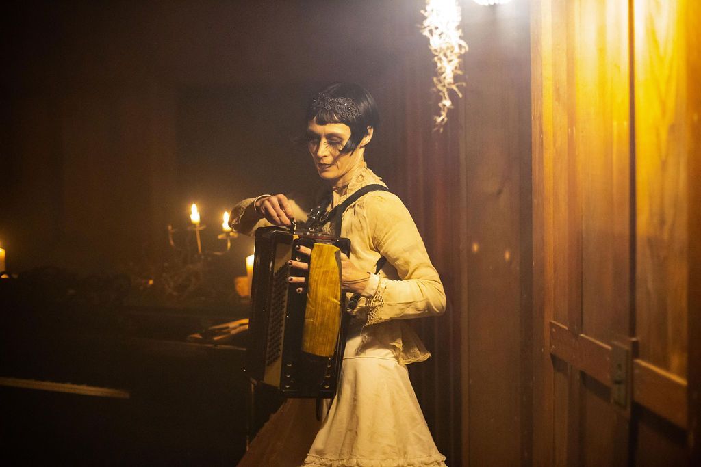 A woman in a white dress is playing an accordion in a dark room.
