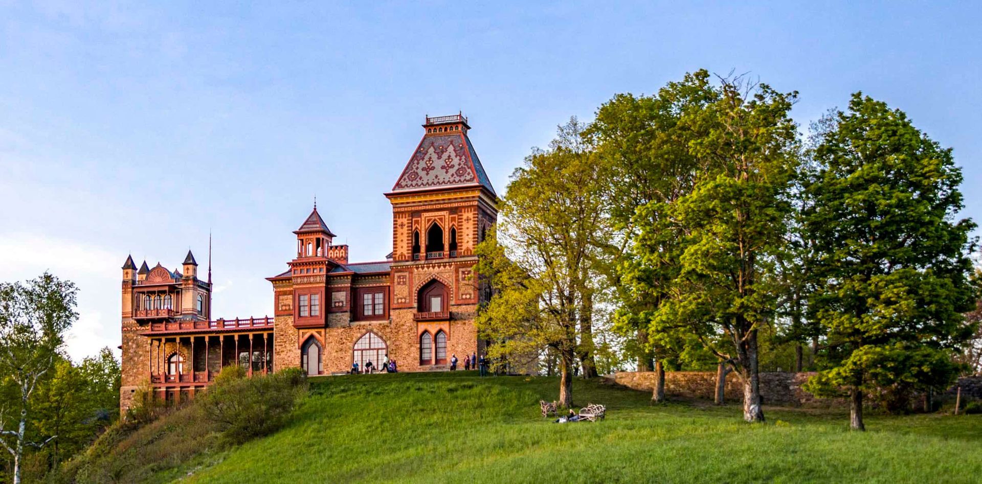 A large castle is sitting on top of a grassy hill surrounded by trees.