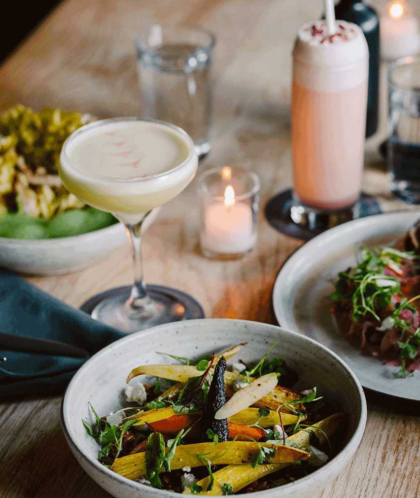 A table topped with plates of food , drinks and candles.