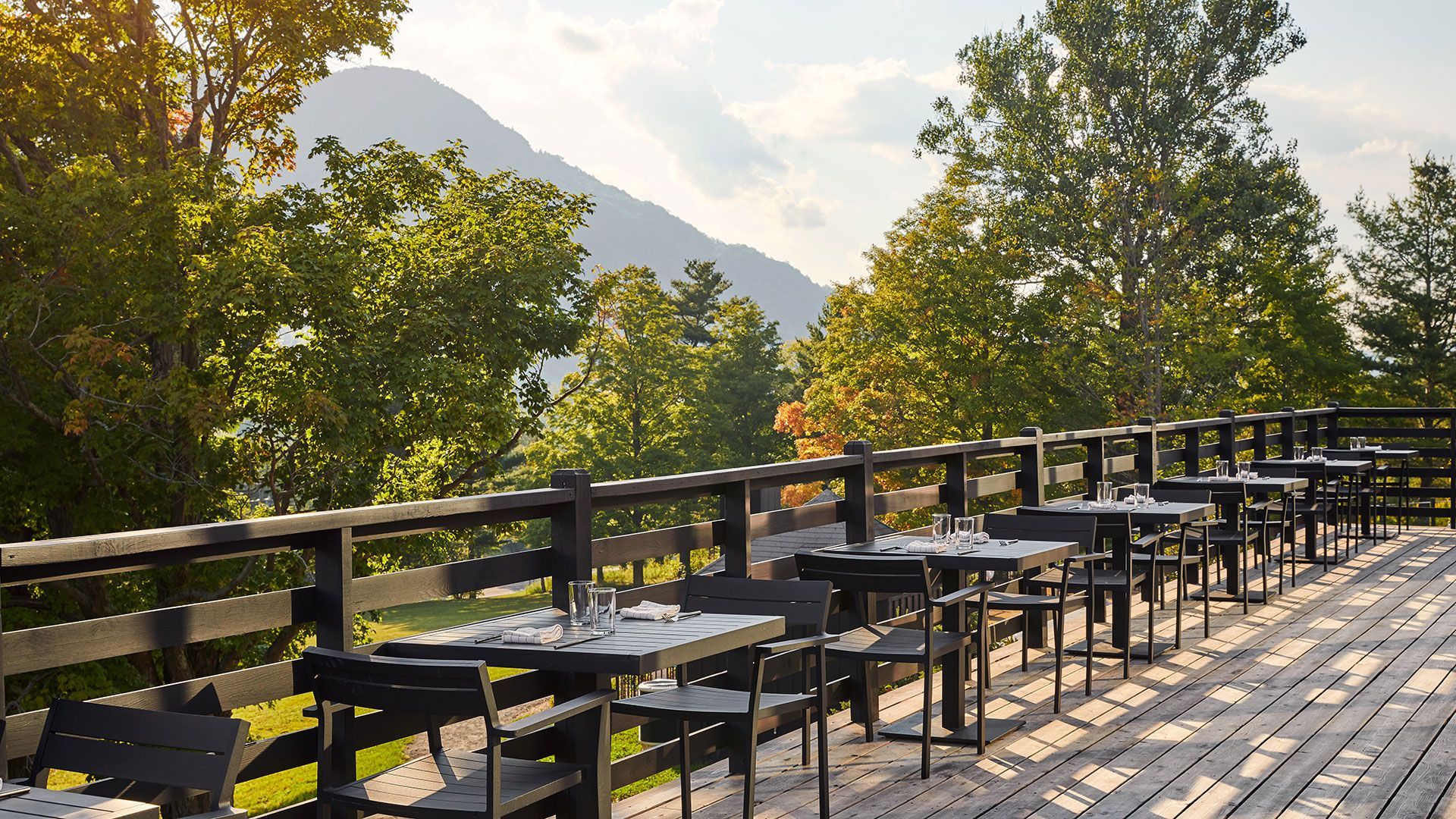 A wooden deck with tables and chairs and a mountain in the background