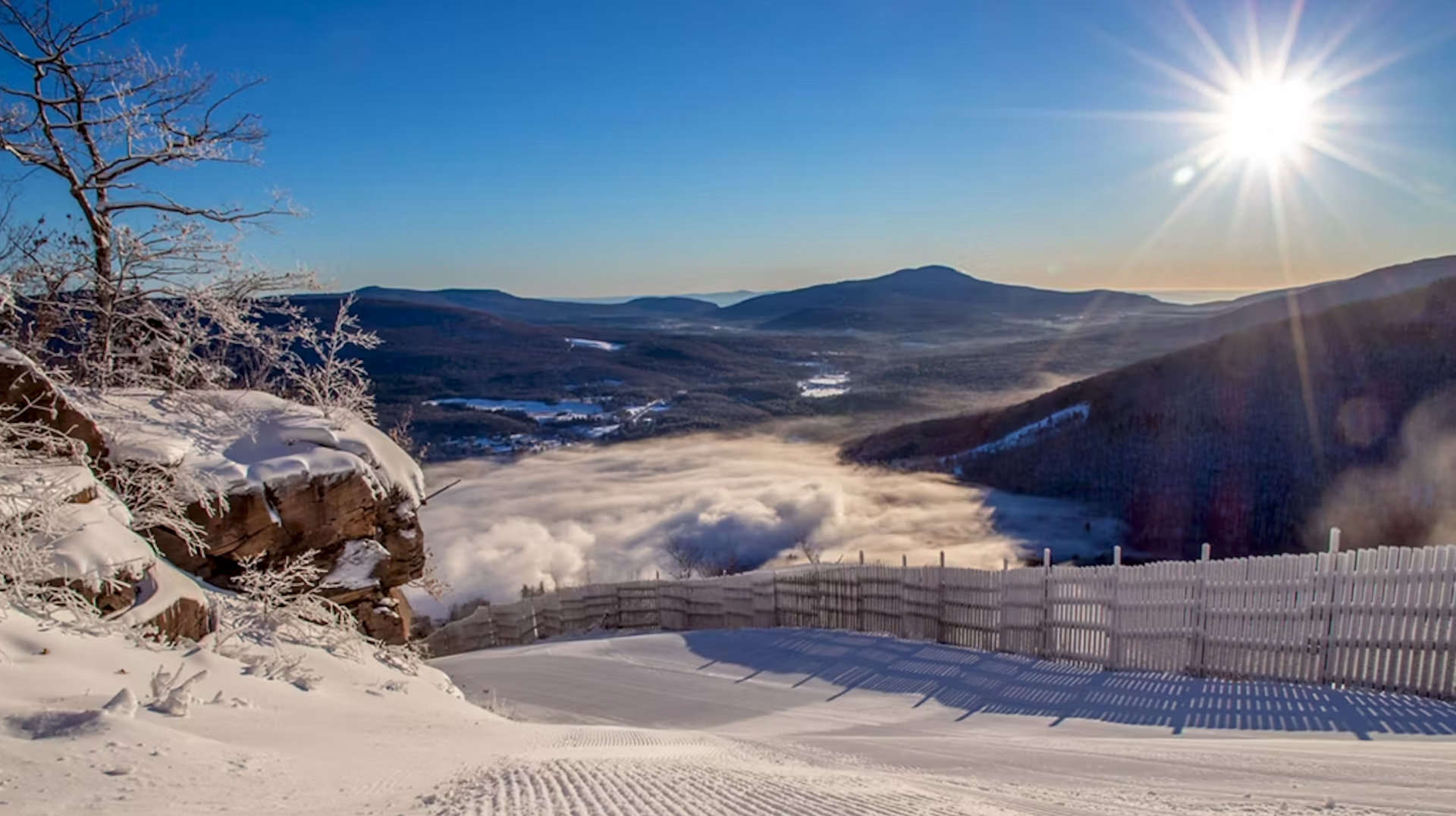 The sun is shining brightly over a snowy landscape with mountains in the background.