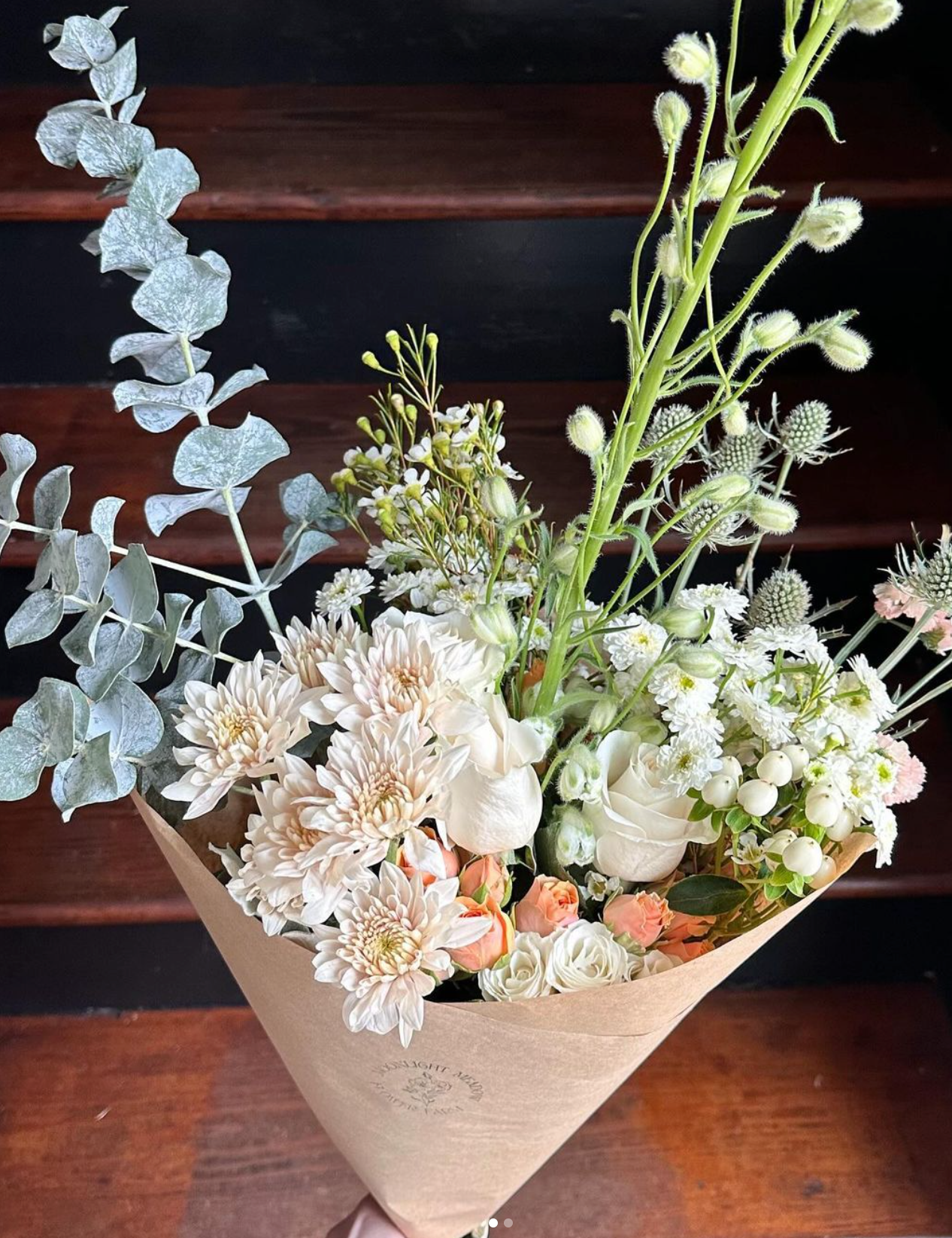 A person is holding a bouquet of flowers wrapped in brown paper.