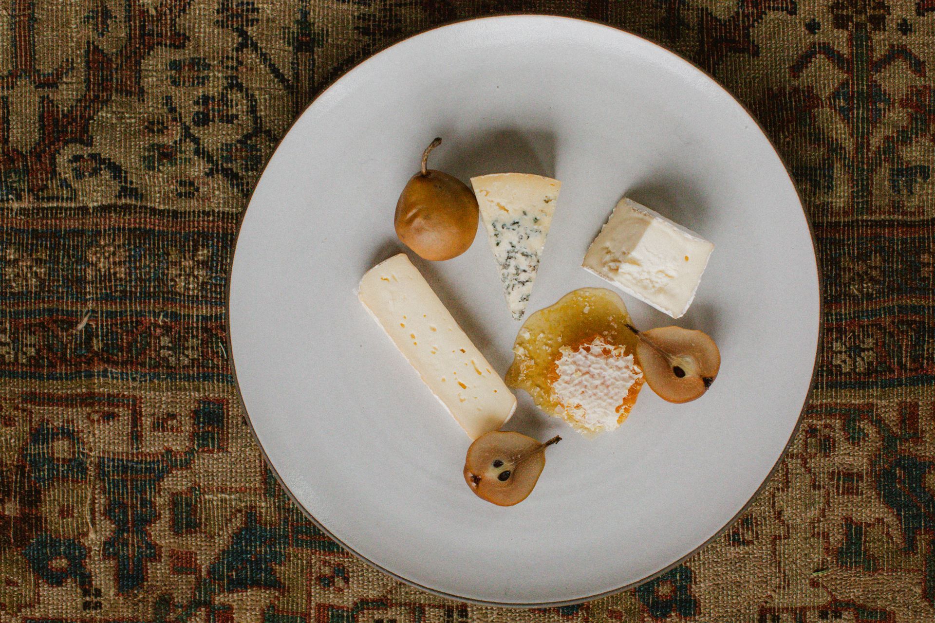 A white plate topped with a variety of cheeses and pears.