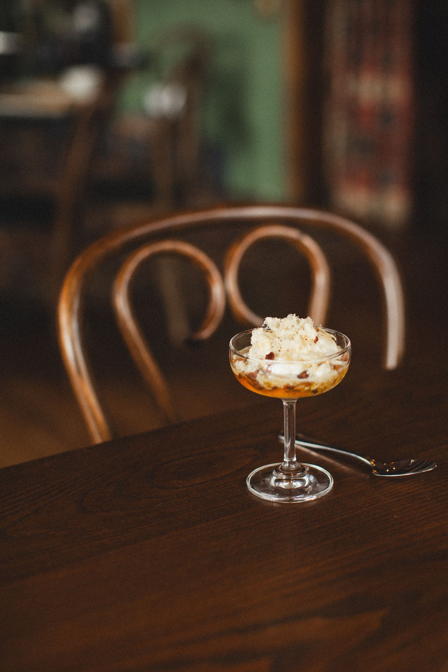 A glass of ice cream is sitting on a wooden table next to a chair.