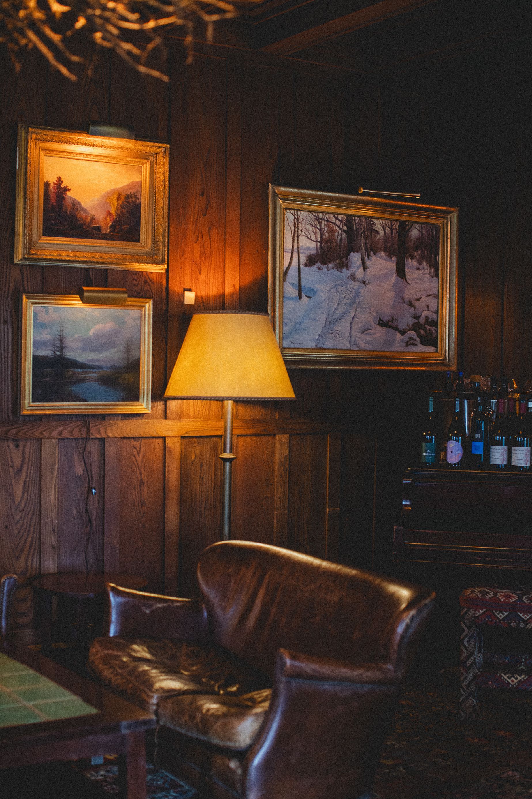 A living room with a couch , chair , lamp and paintings on the wall
