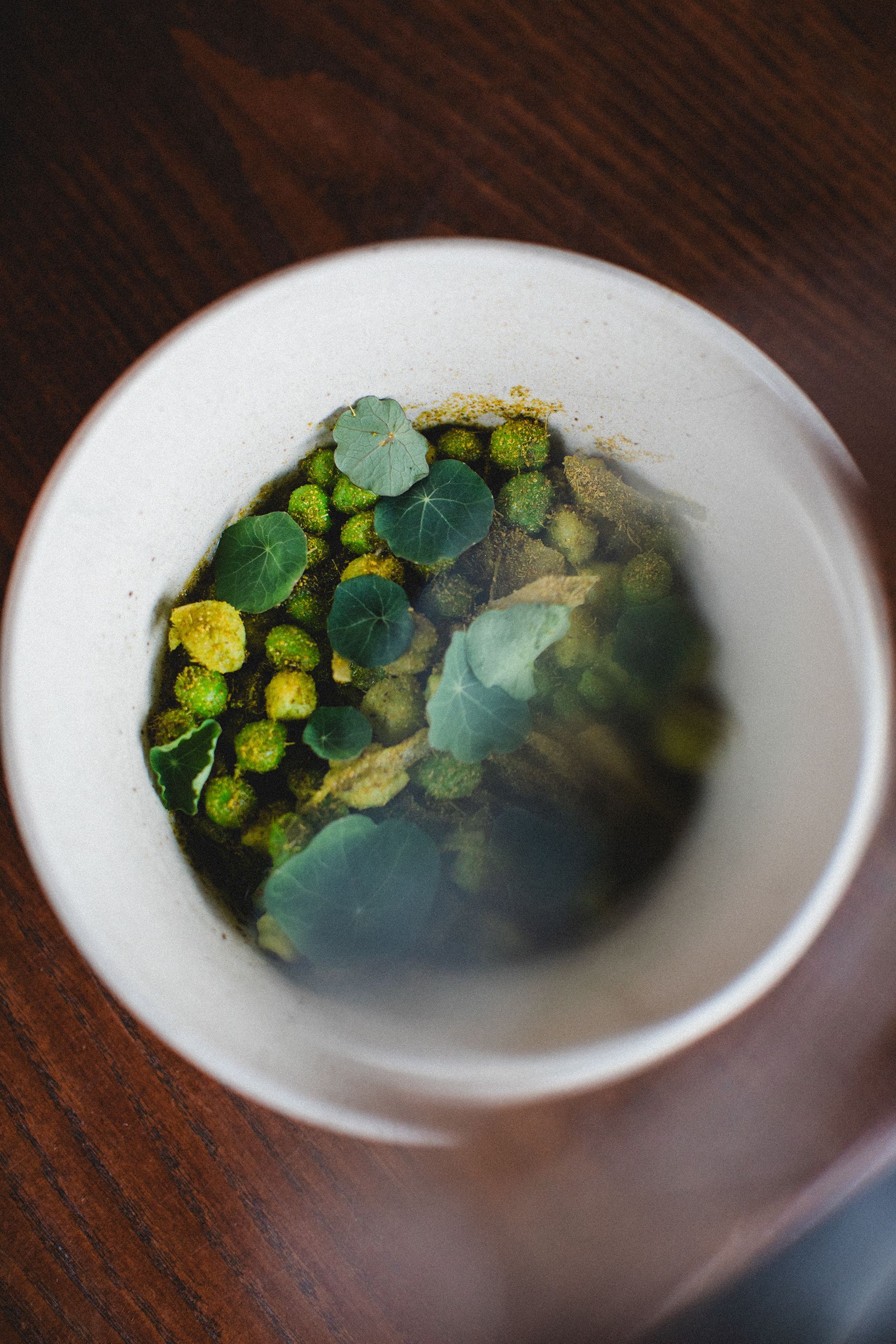 A bowl of green vegetables is sitting on a wooden table.