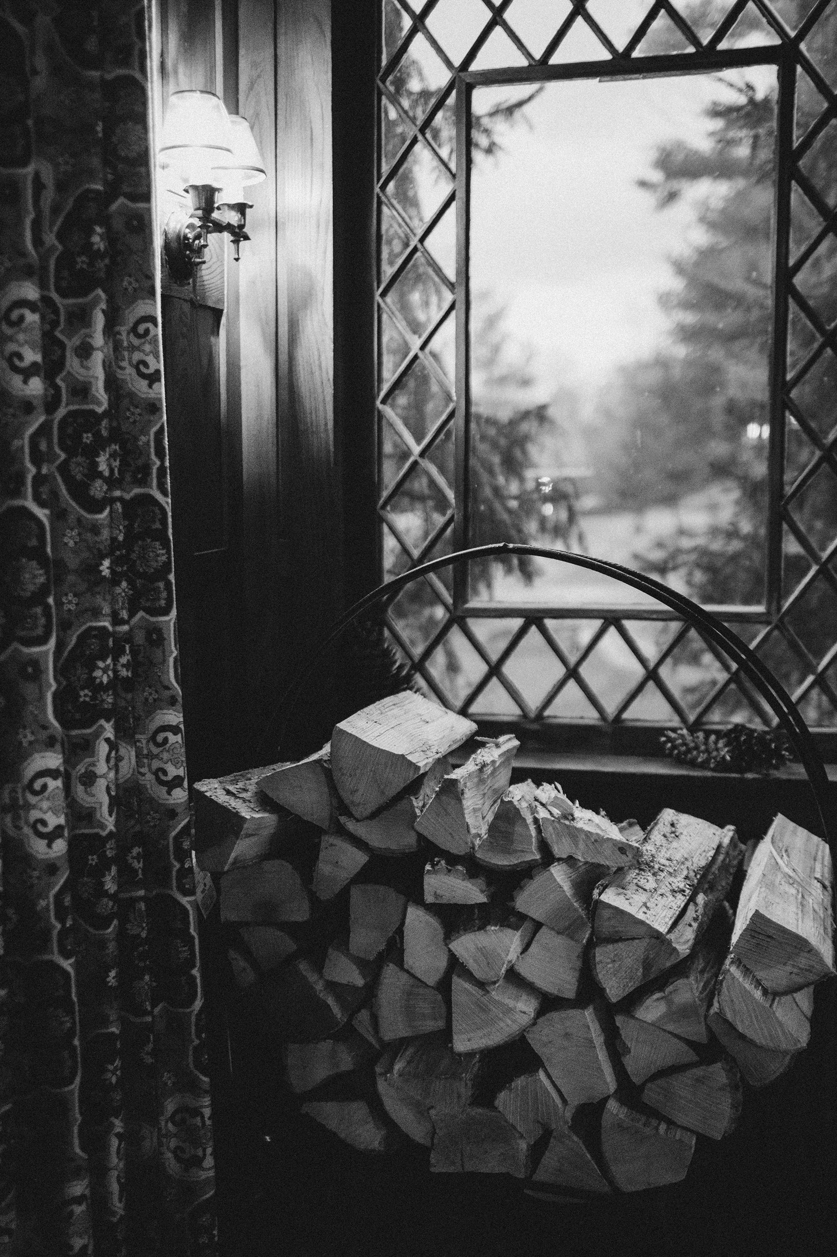 A black and white photo of a pile of logs in front of a window