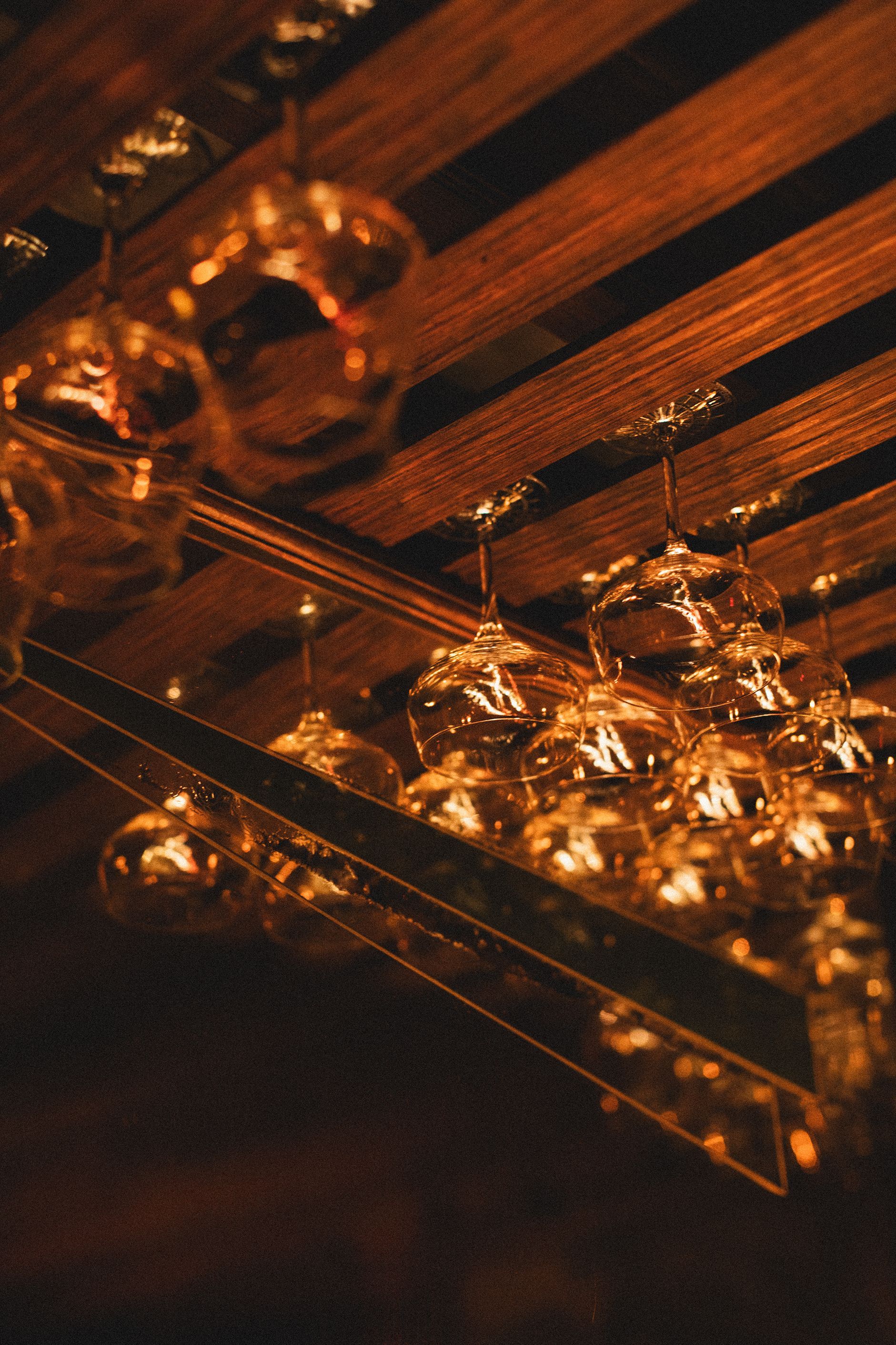 A bunch of wine glasses hanging from a wooden ceiling.
