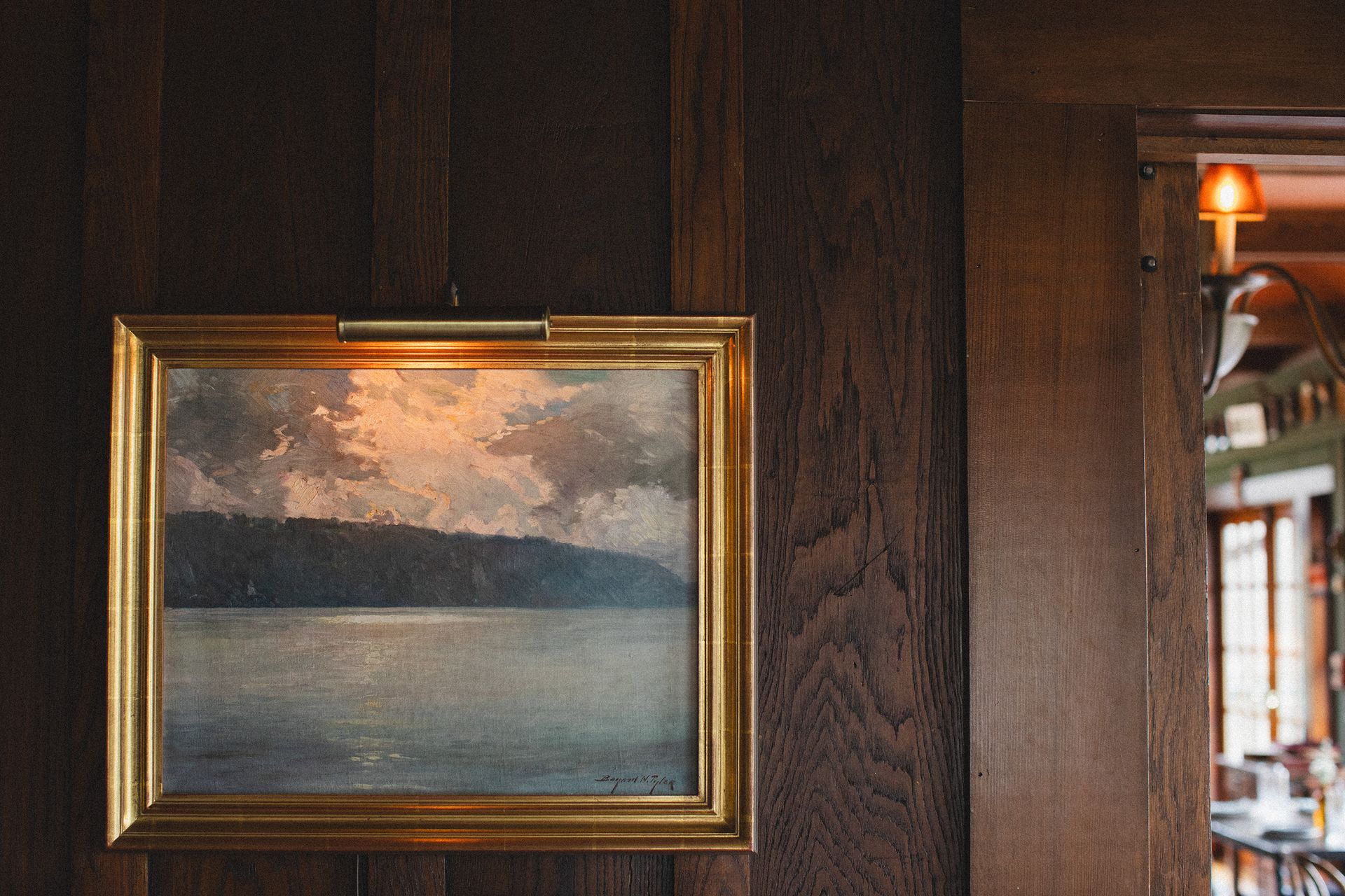 A painting of a lake is hanging on a wooden wall.