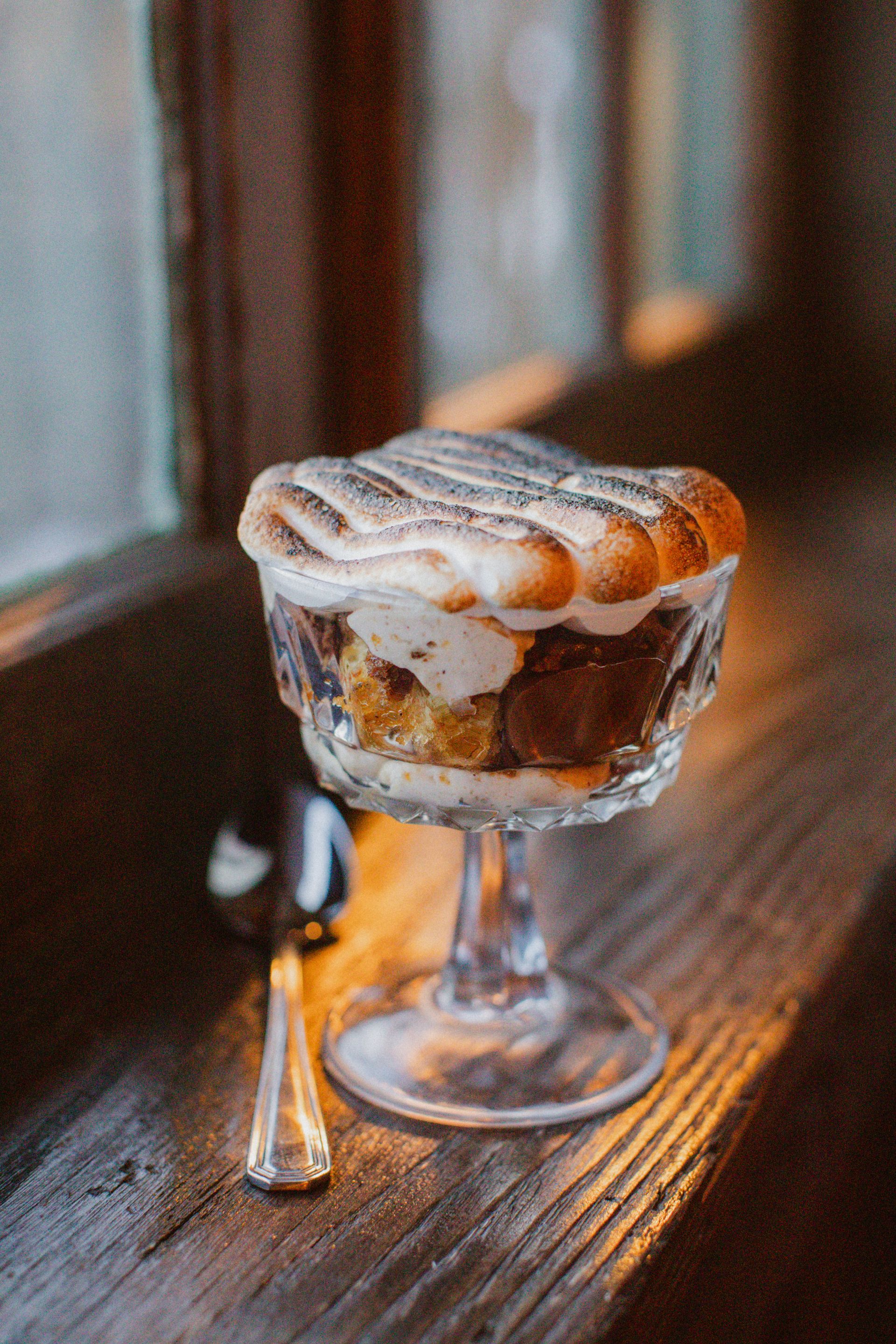 A dessert in a glass bowl with a spoon on a wooden table.