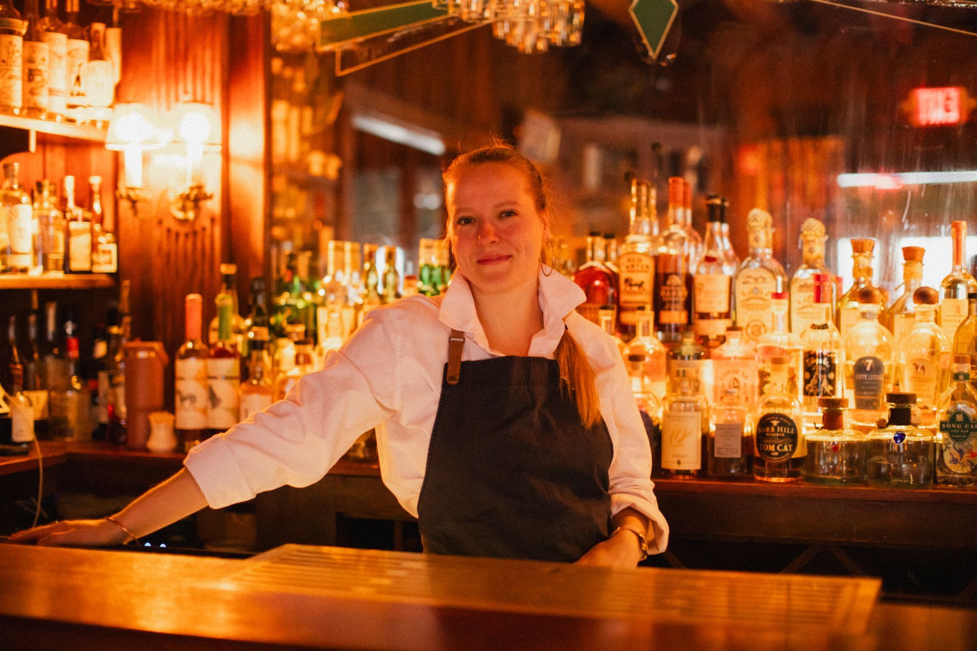 A woman in an apron is standing behind a bar.