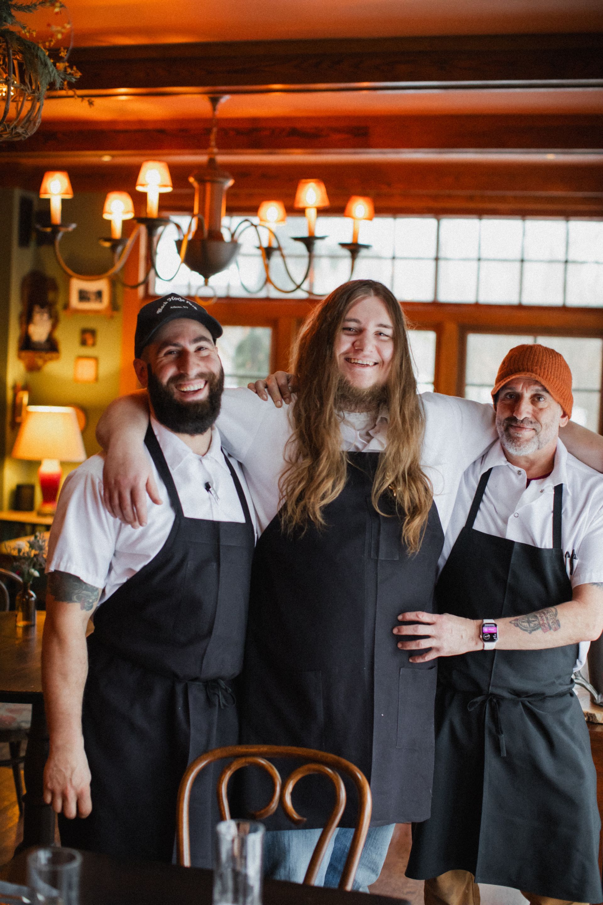 Three men in aprons are posing for a picture in a restaurant.
