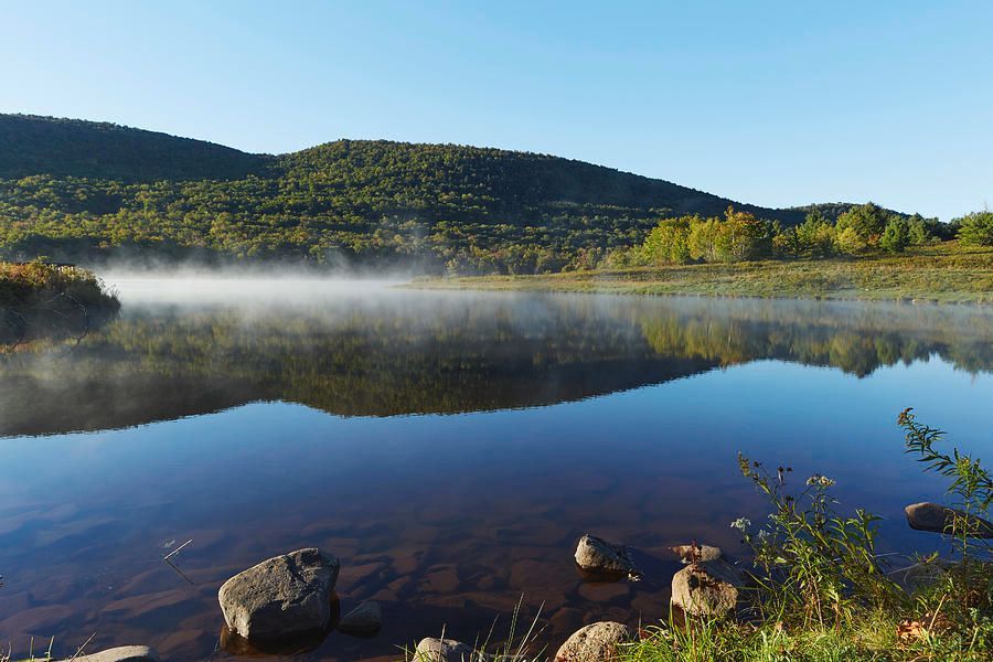 A lake with fog coming out of it and mountains in the background