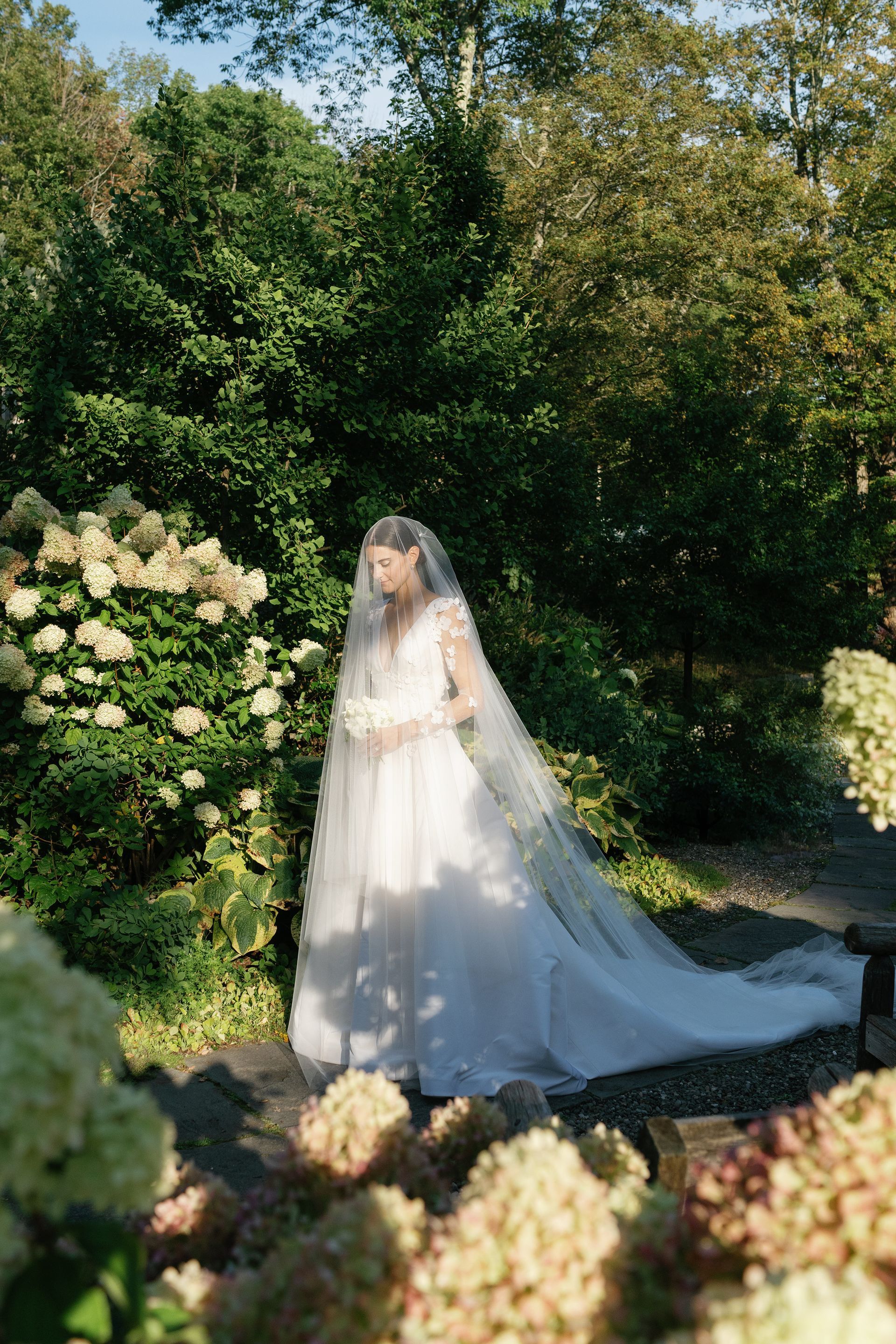 A bride in a wedding dress and veil is standing in a garden.