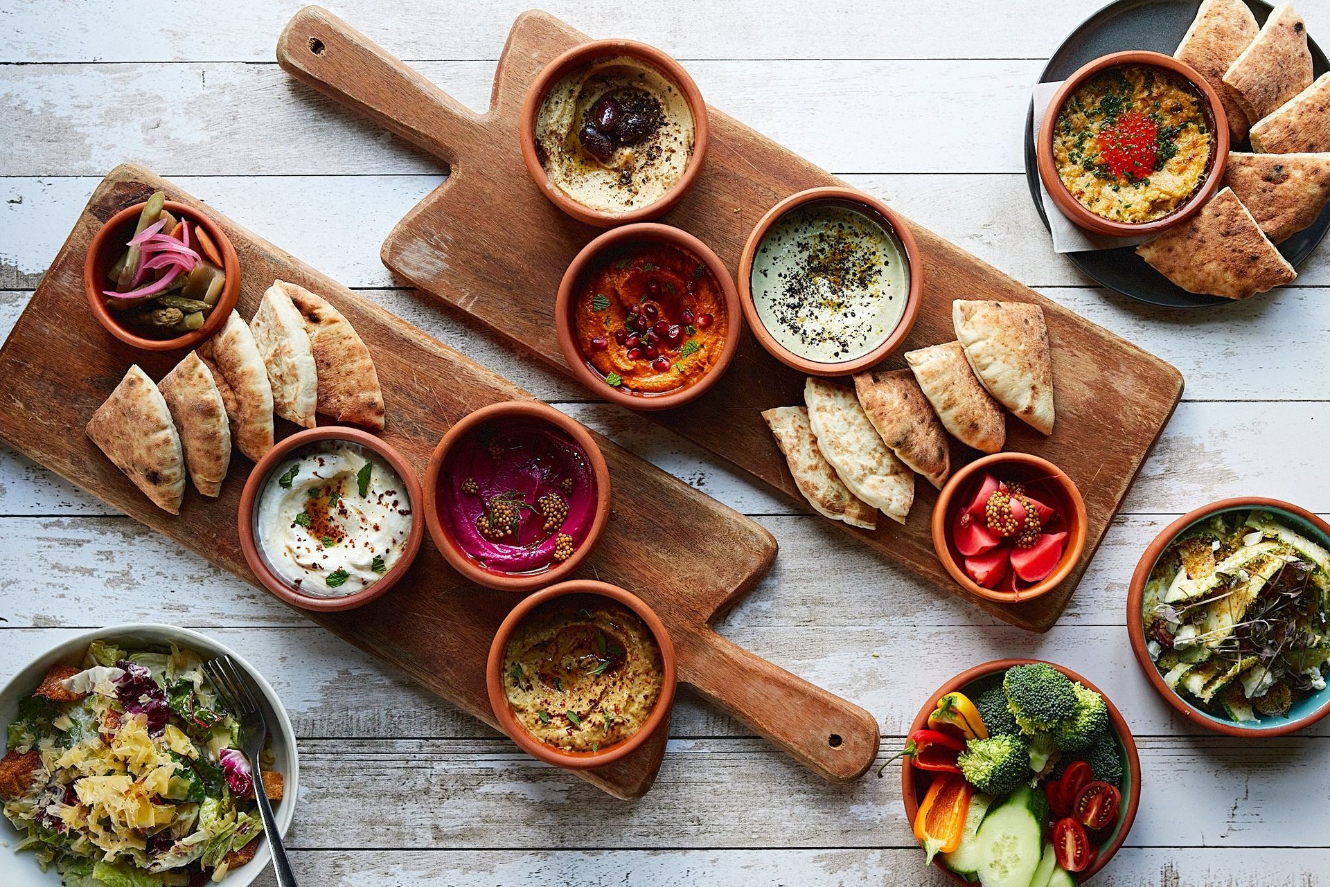 A wooden cutting board topped with bowls of food and bread.