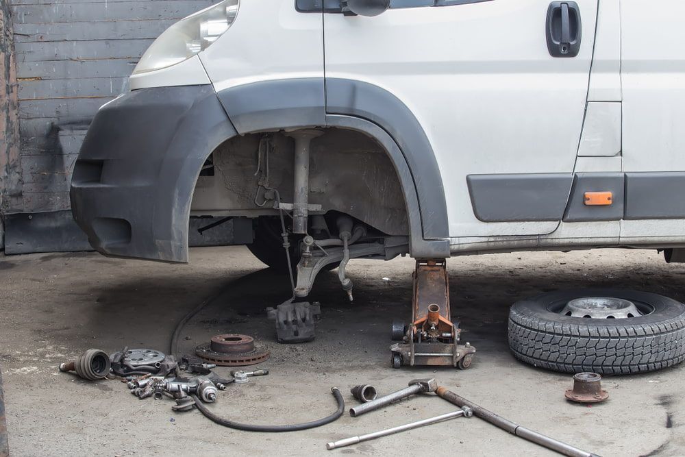 A White Van is Sitting on a Jack in a Garage — C & C Panel & Paint Mackay In Mackay, QLD