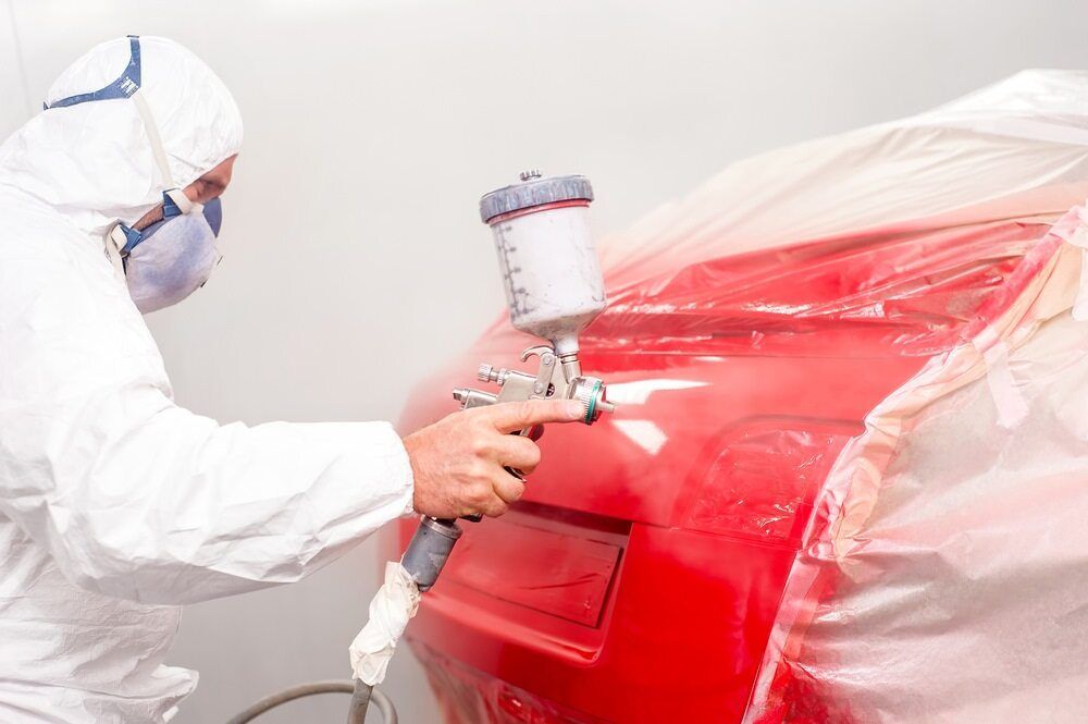 A Man in a Protective Suit is Spray Painting a Red Car — C & C Panel & Paint Mackay In Mackay, QLD