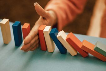 Hand stopping a row of colorful dominoes from falling on a blue surface