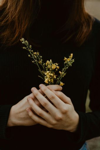 Hands holding a small sprig of yellow flowers against a dark top.