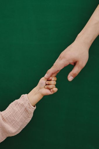 Adult hand holding a child's hand against a green background