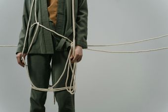 Person in a green outfit wrapped in rope against a plain gray background