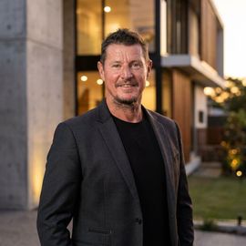 Man in a dark blazer standing outside a modern building at dusk