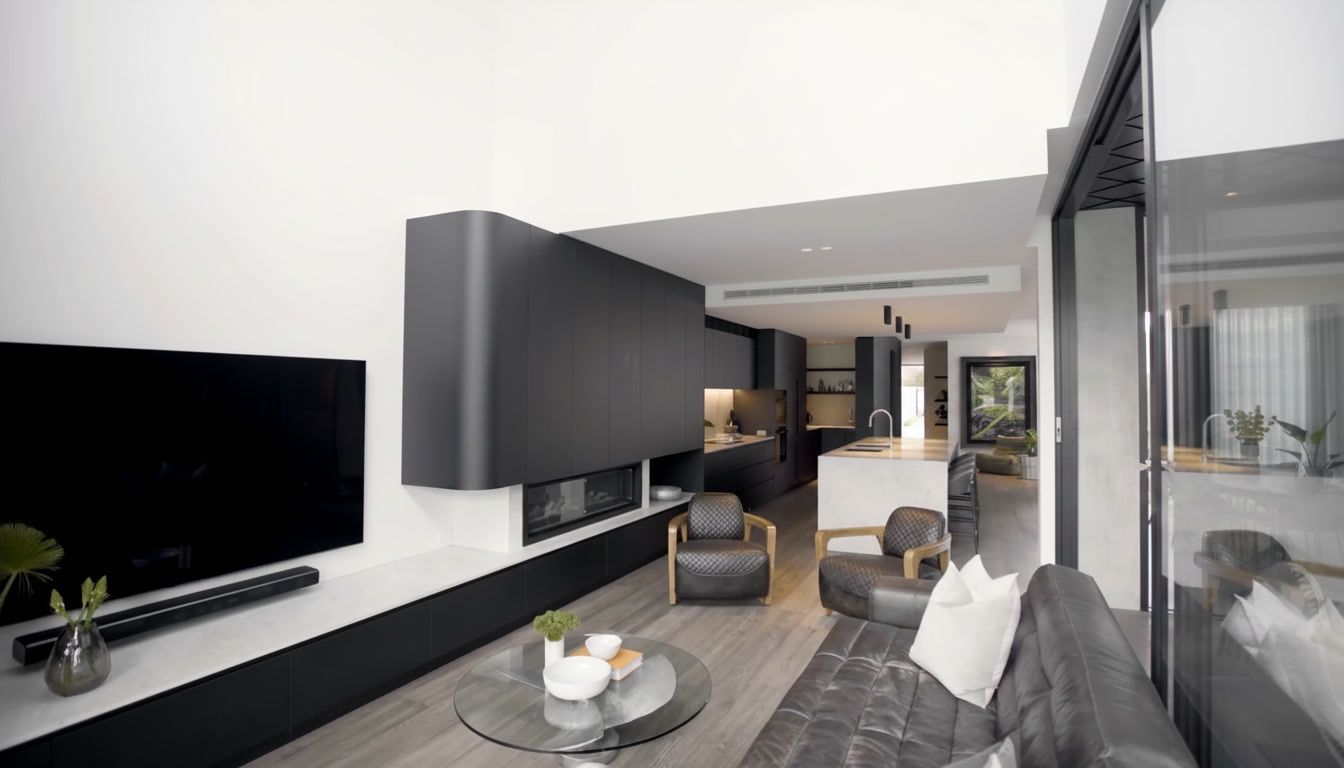 Modern minimalist living room with gray sofas, black TV wall, and open view to a dining area