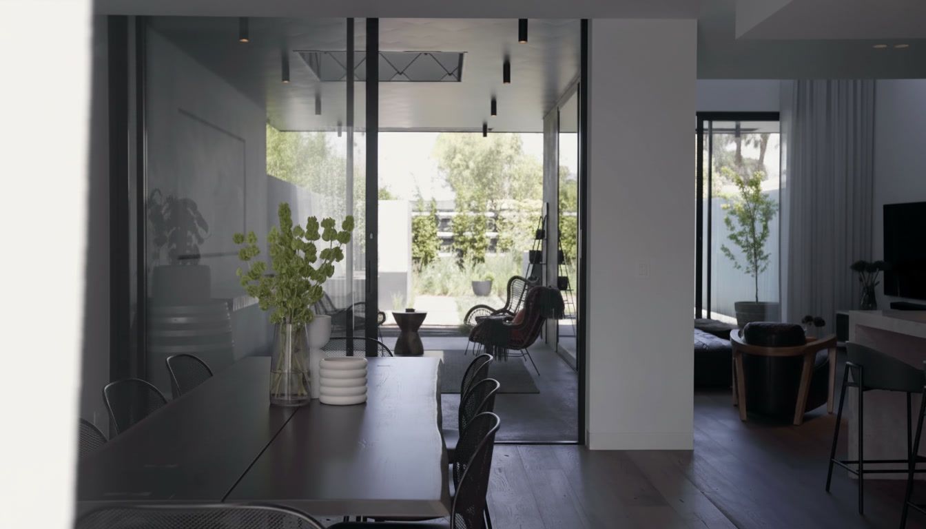 Modern office interior with glass walls, desks, chairs, and a person seated by a bright window.