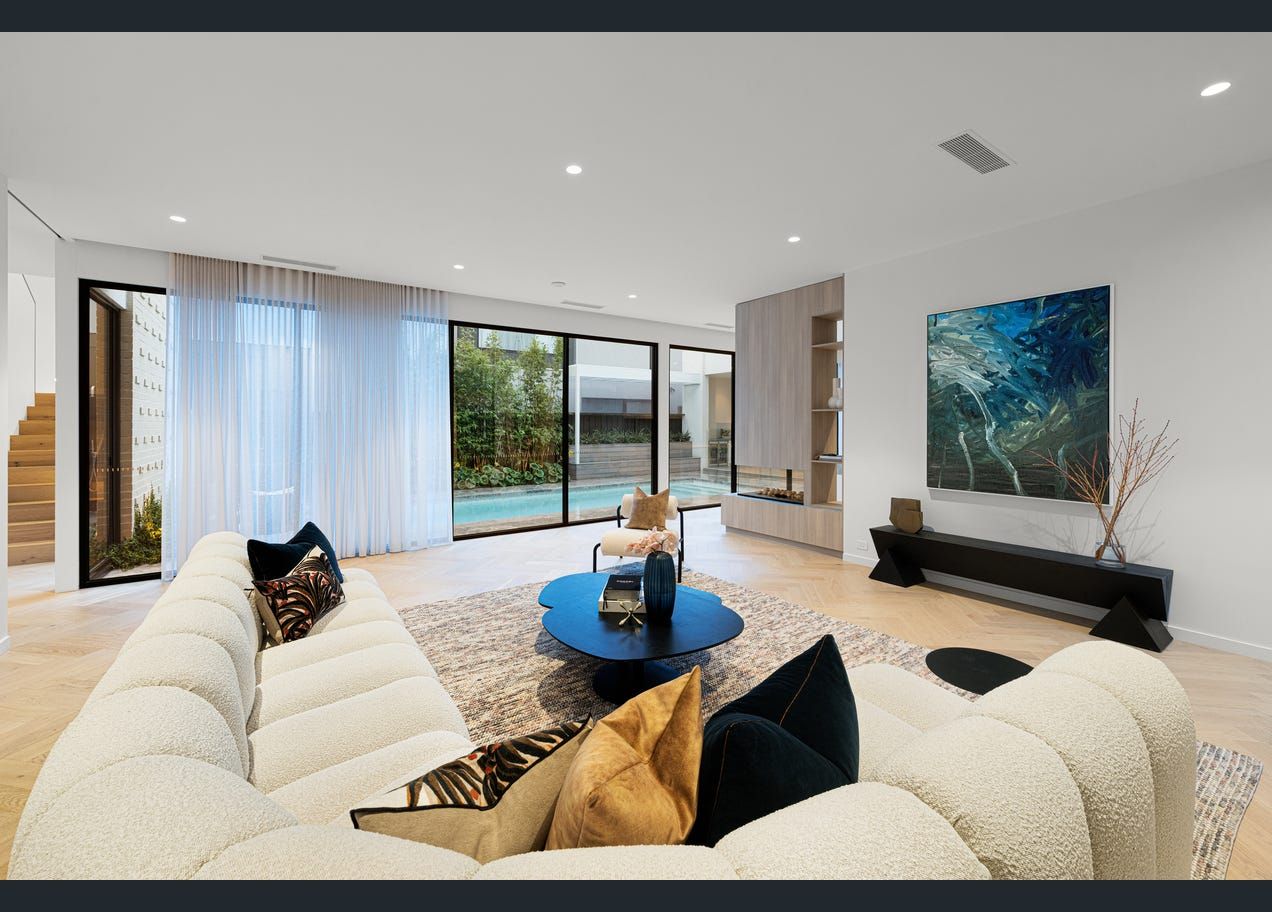 Bright modern living room with cream sofas, blue accents, large windows, and abstract wall art.